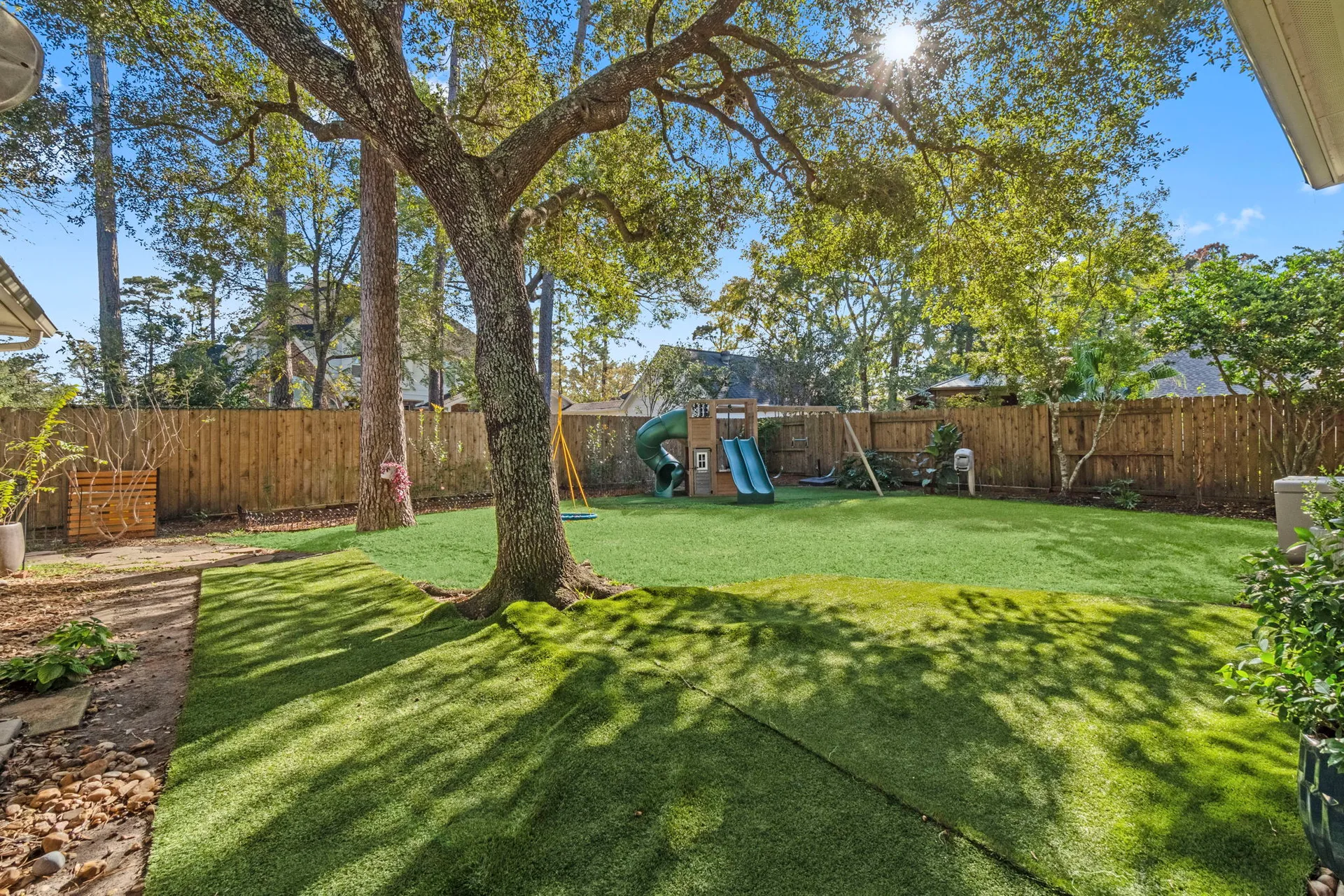 Fenced backyard with artificial turf lawn, mature tree, and wood privacy fencing