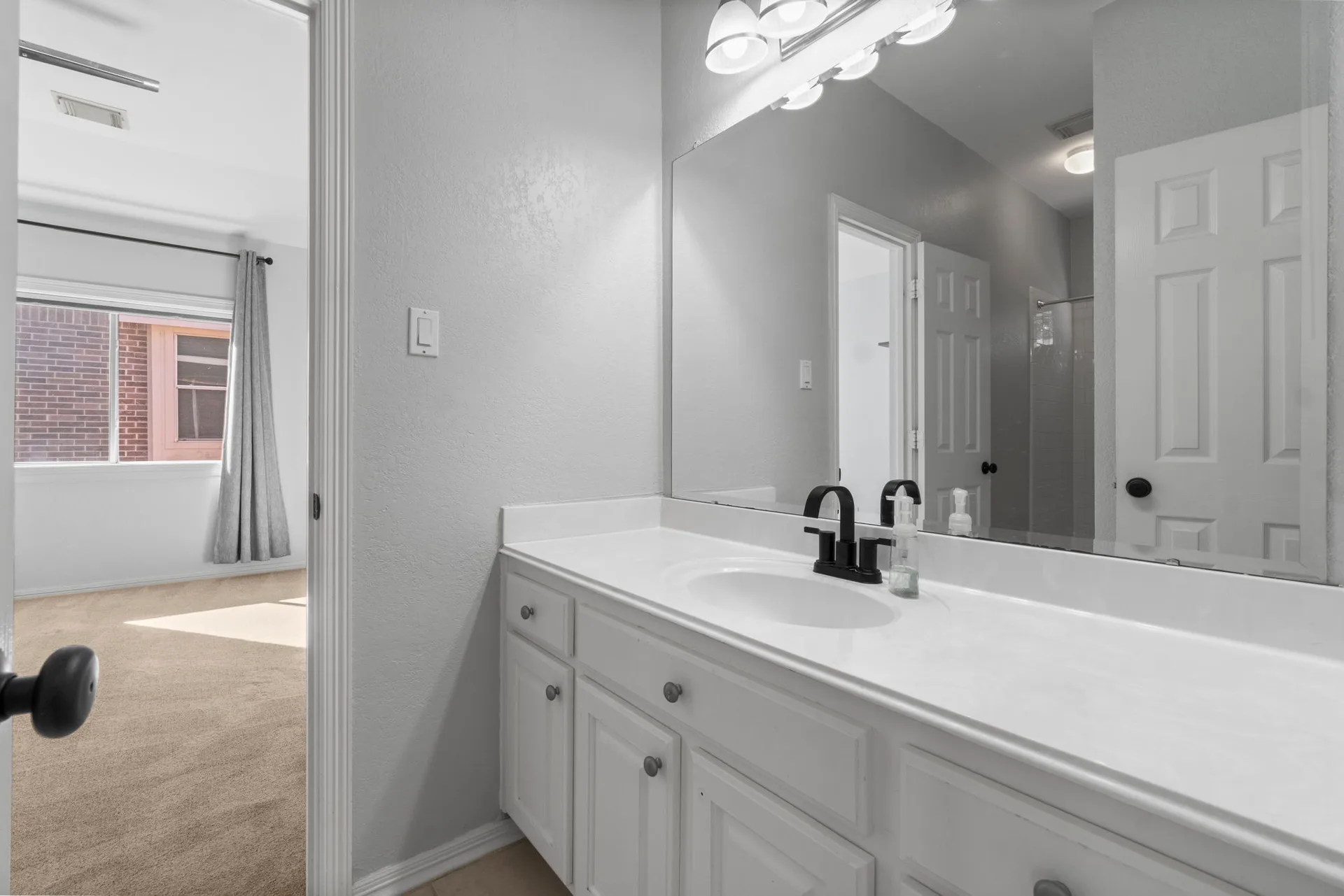 Bathroom vanity with white vanity, matte black faucet, and full-width mirror