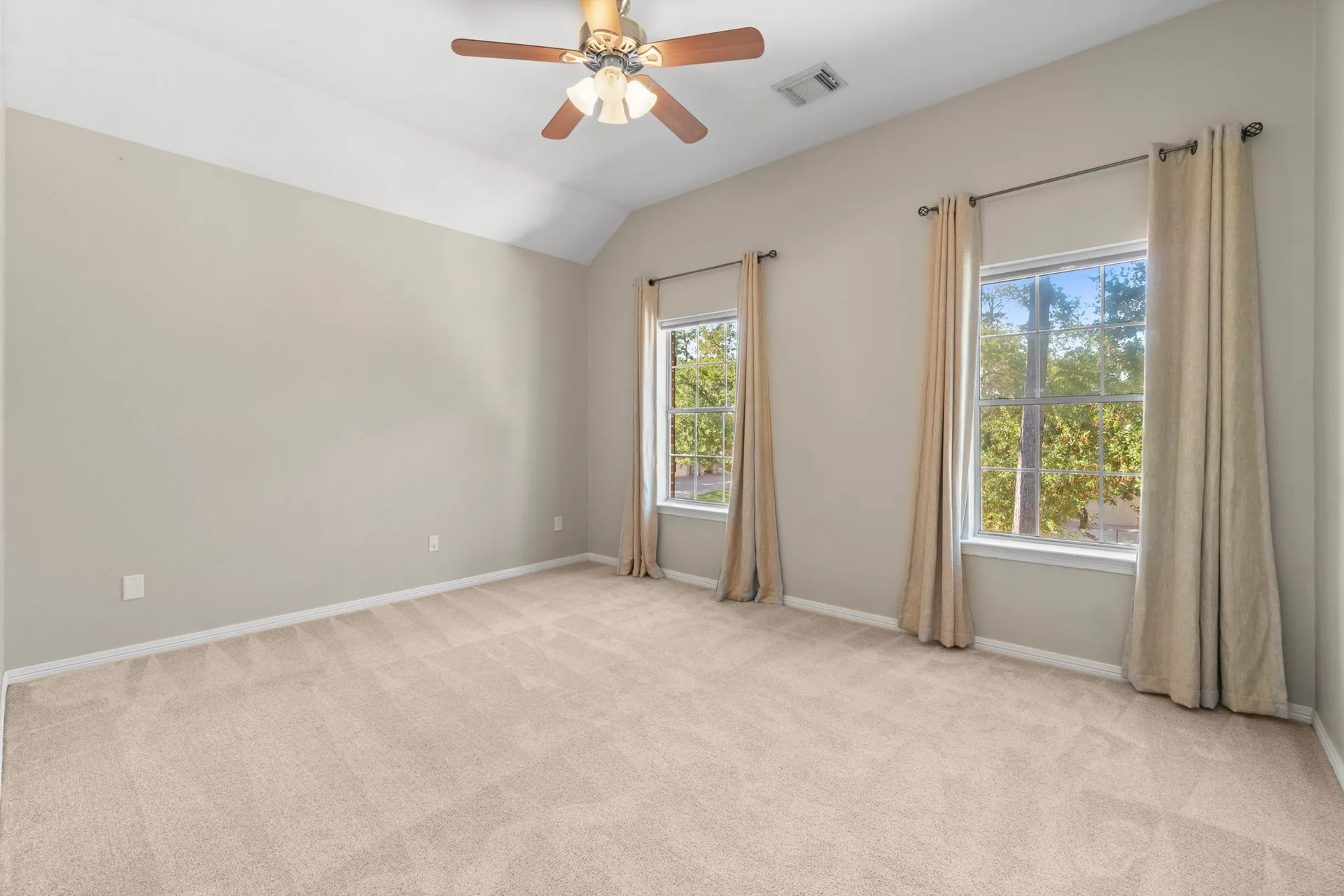 Bedroom with beige wall paint, light carpet, and vaulted ceiling
