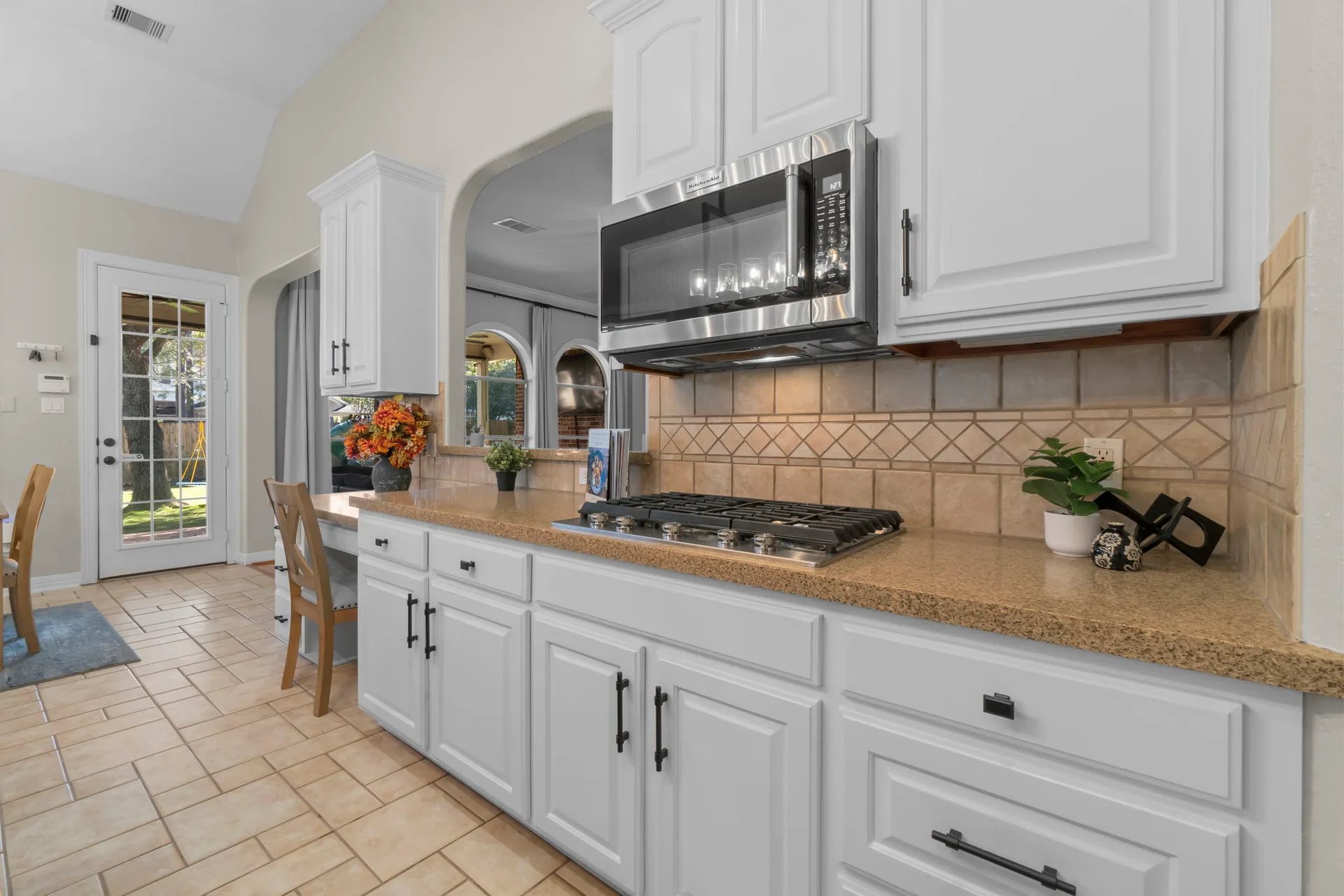 Kitchen cooktop and pass-through window with white Shaker cabinets and granite counters