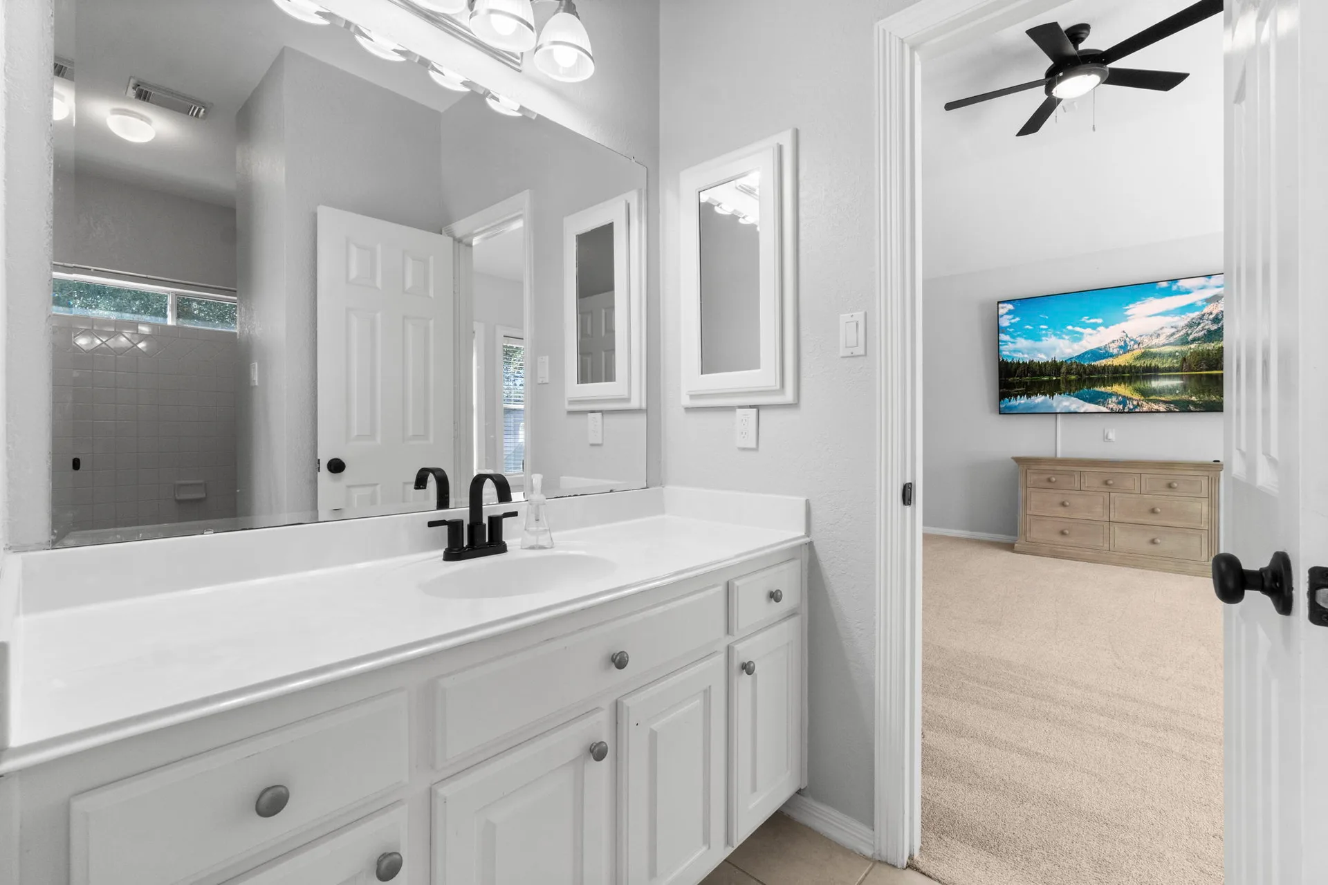 Bathroom looking into adjacent bedroom with white cabinetry and matte black faucet