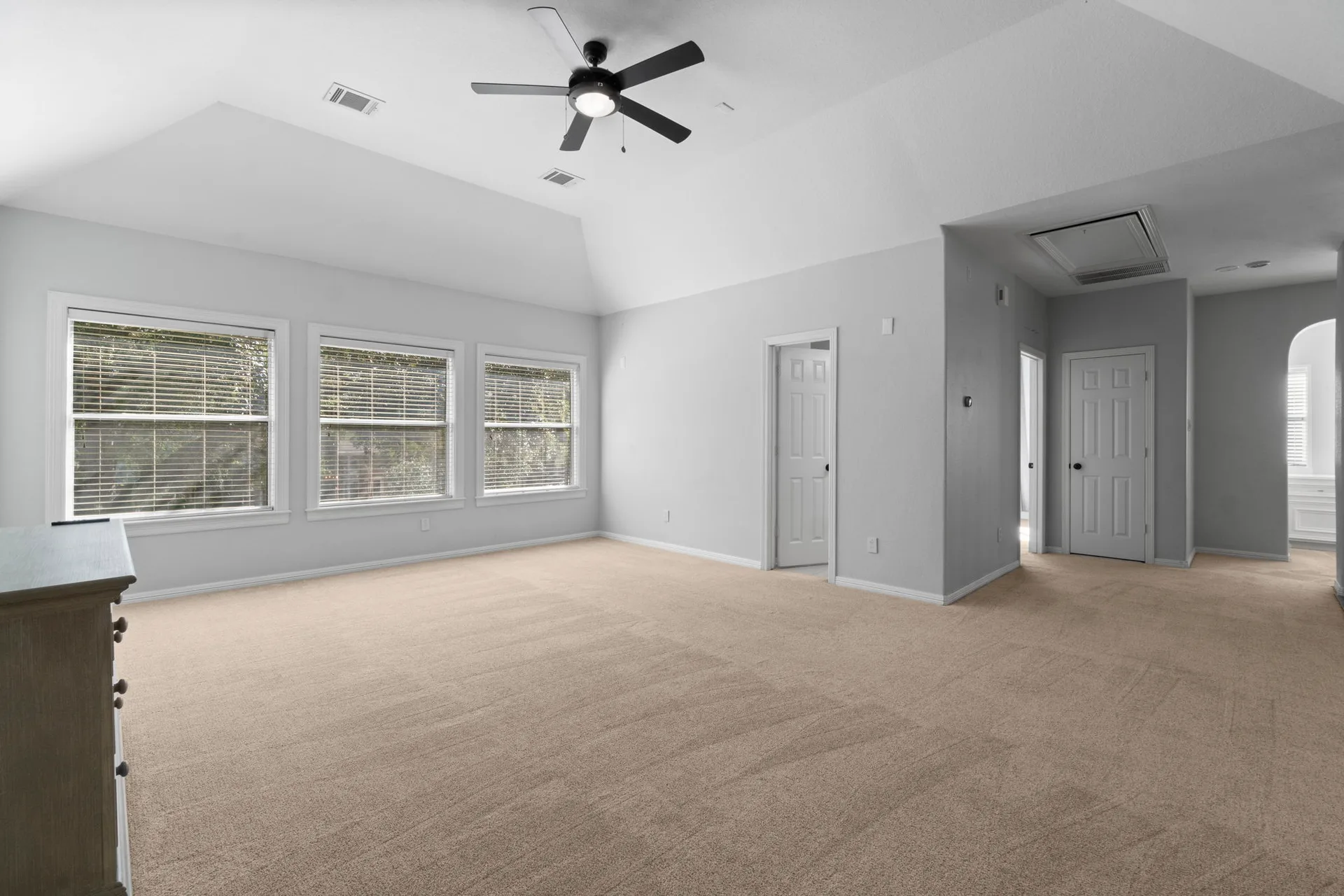 Primary bedroom with vaulted ceiling, triple window bank, and beige carpeting