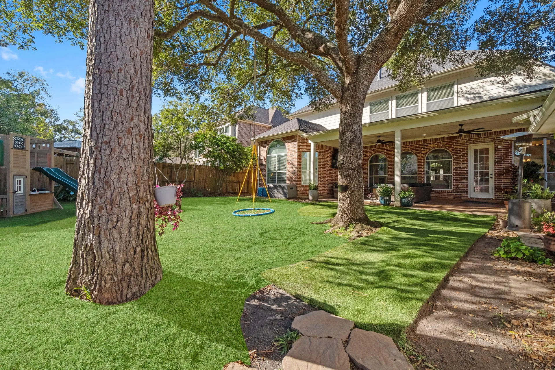 Backyard facing home showing covered patio, brick architecture, and tree swing