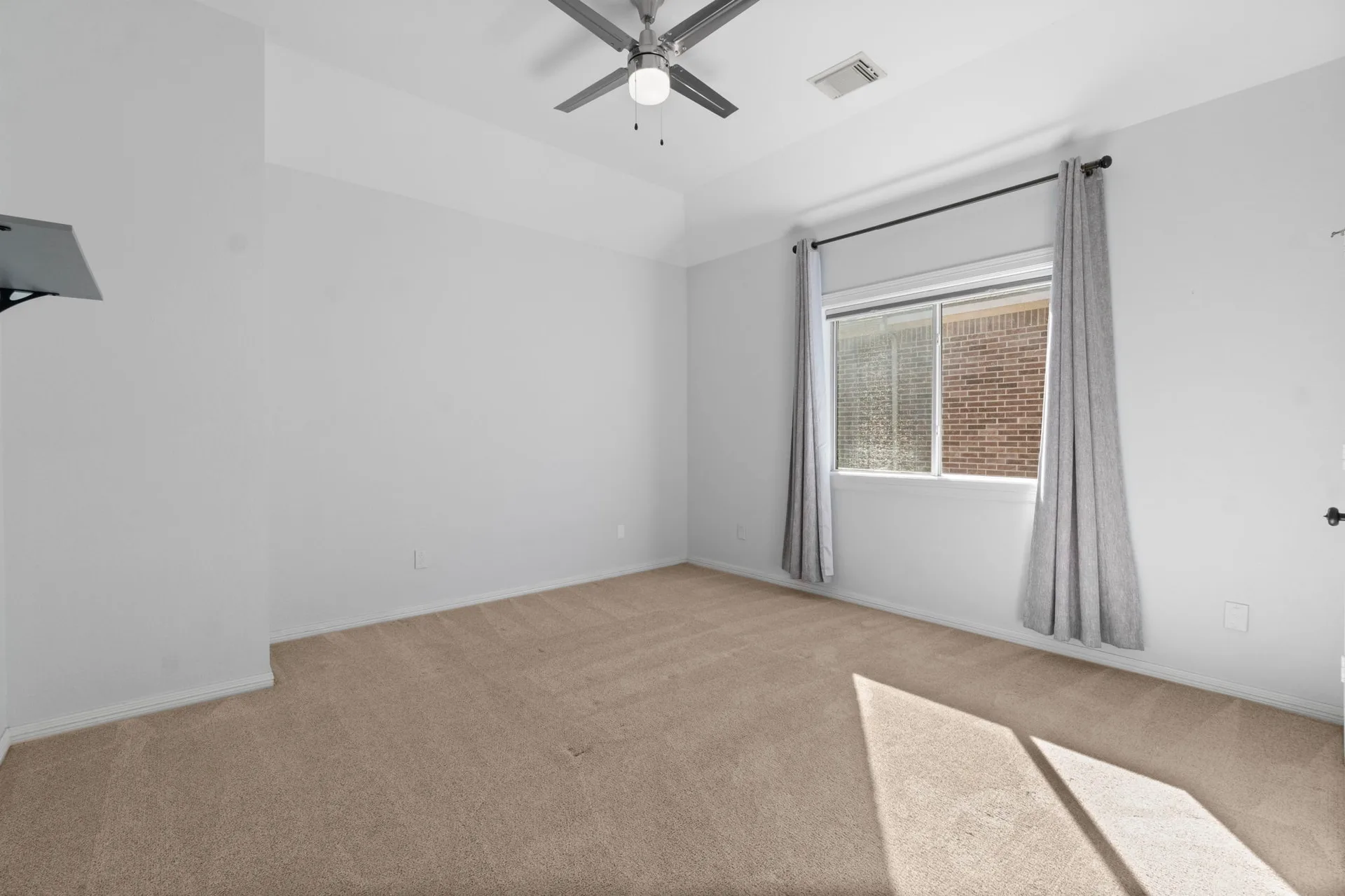 Secondary bedroom with beige carpeting, light grey walls, and natural sunlight
