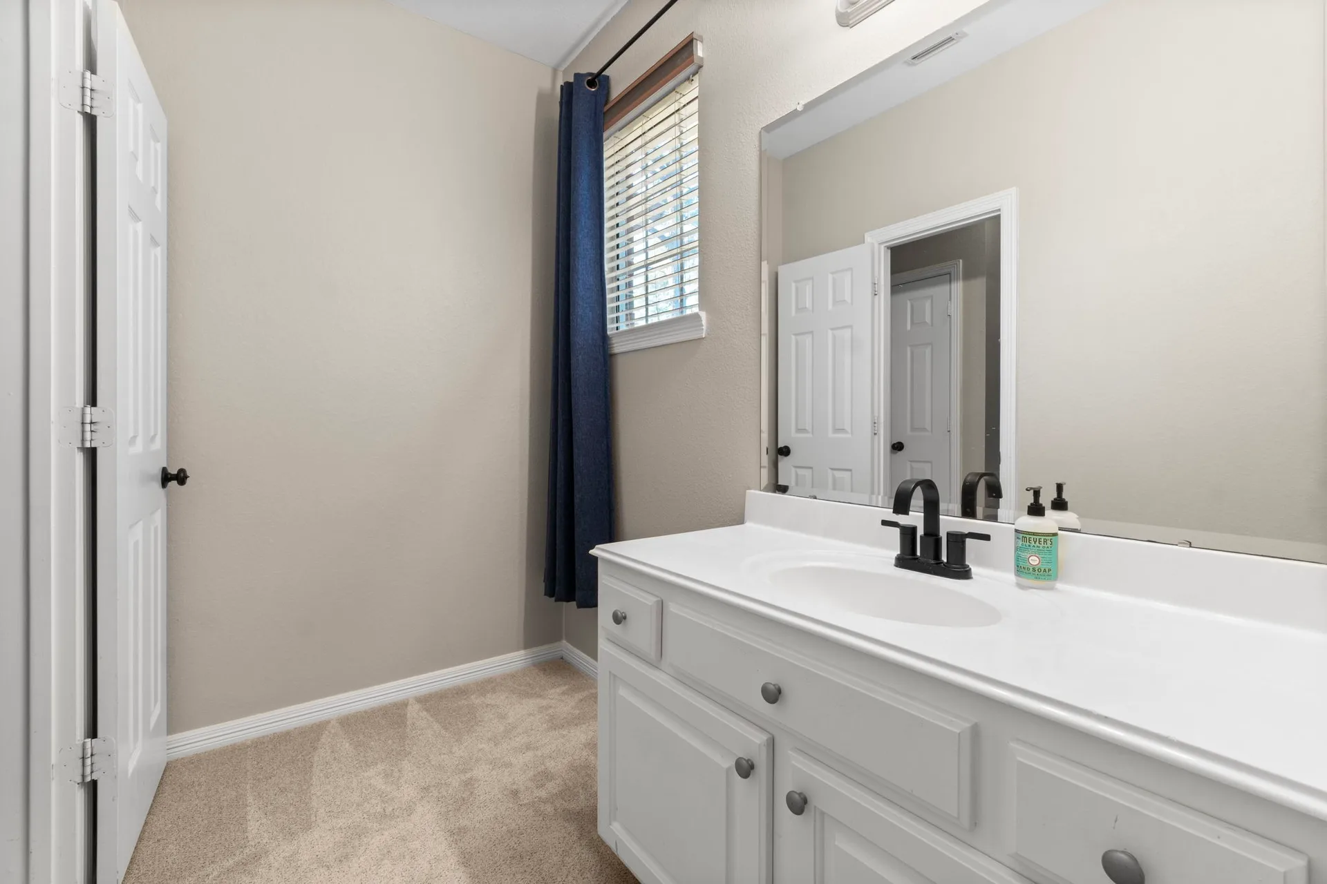 Bathroom vanity with white cabinetry, integrated countertop, and matte black faucet