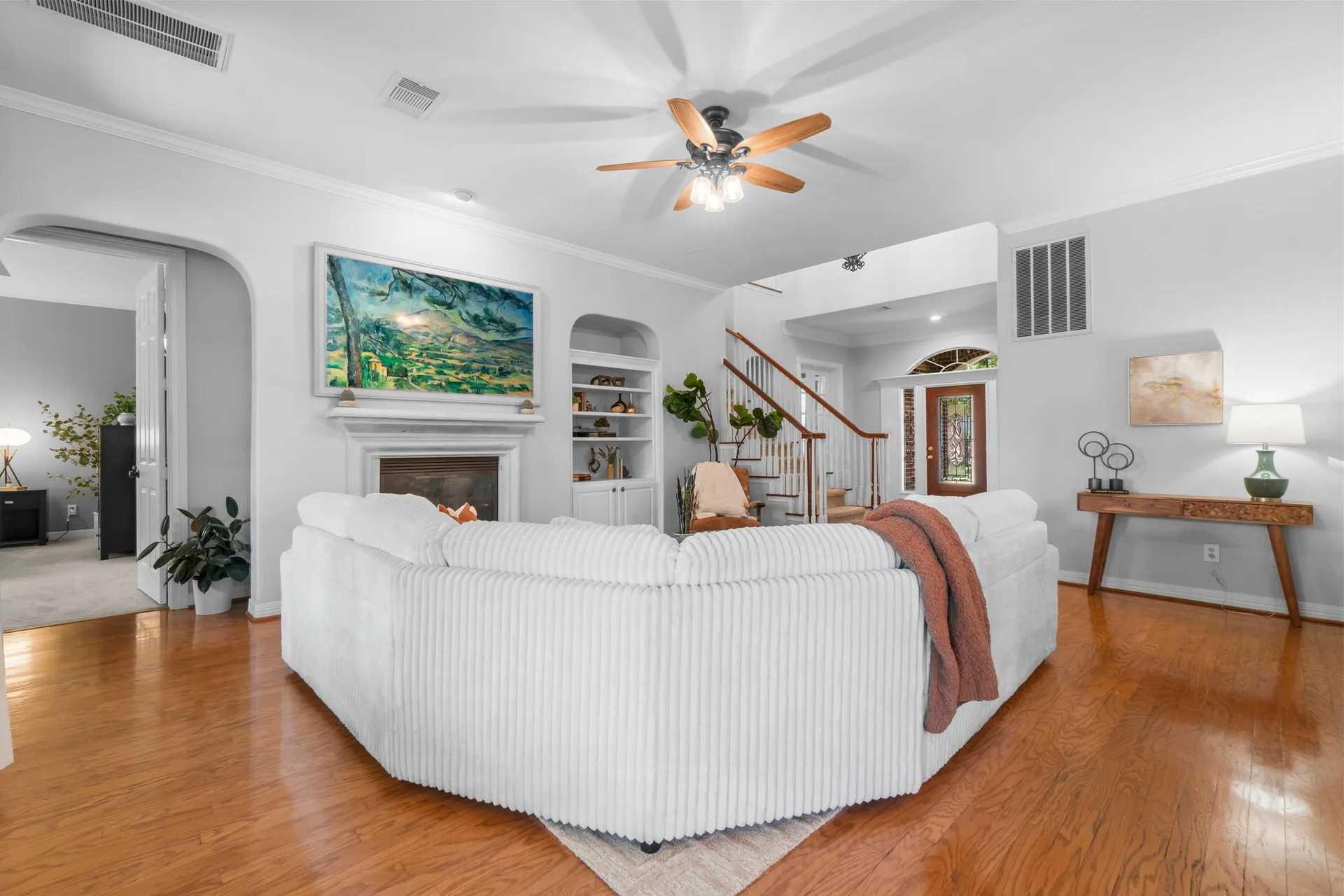 Living room with fireplace, staircase in background, arched doorways, and hardwood floors