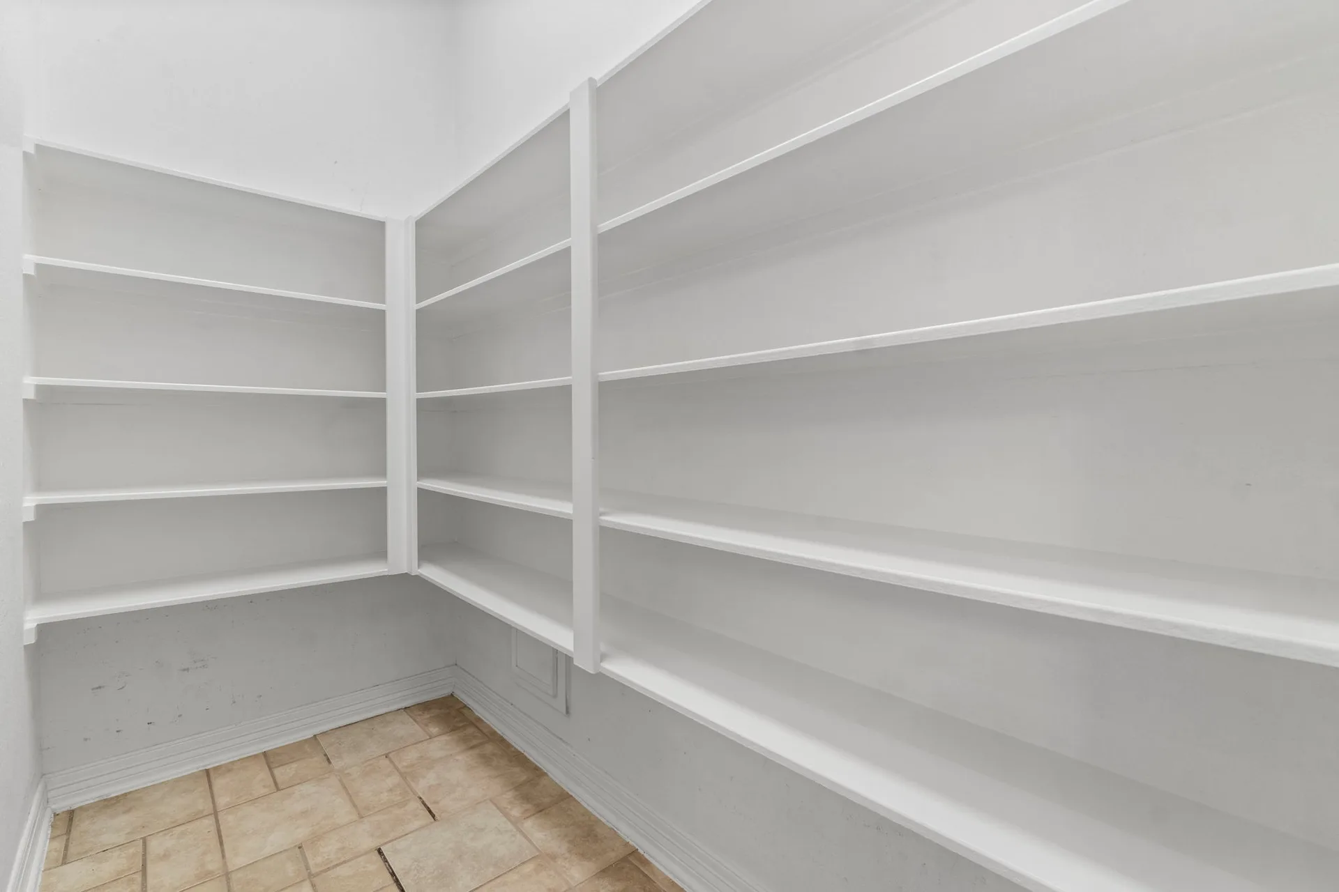 Walk-in kitchen pantry with white wooden shelving and tile flooring