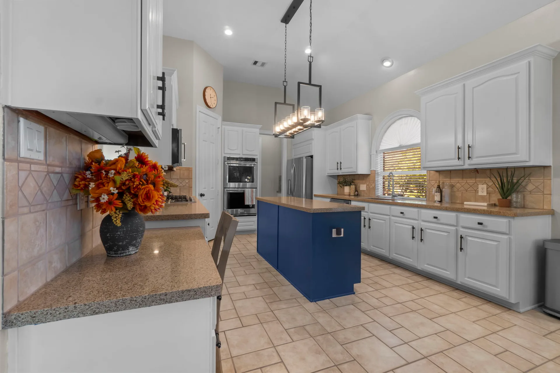 Kitchen with white raised-panel cabinetry, navy blue island, and geometric pendant light