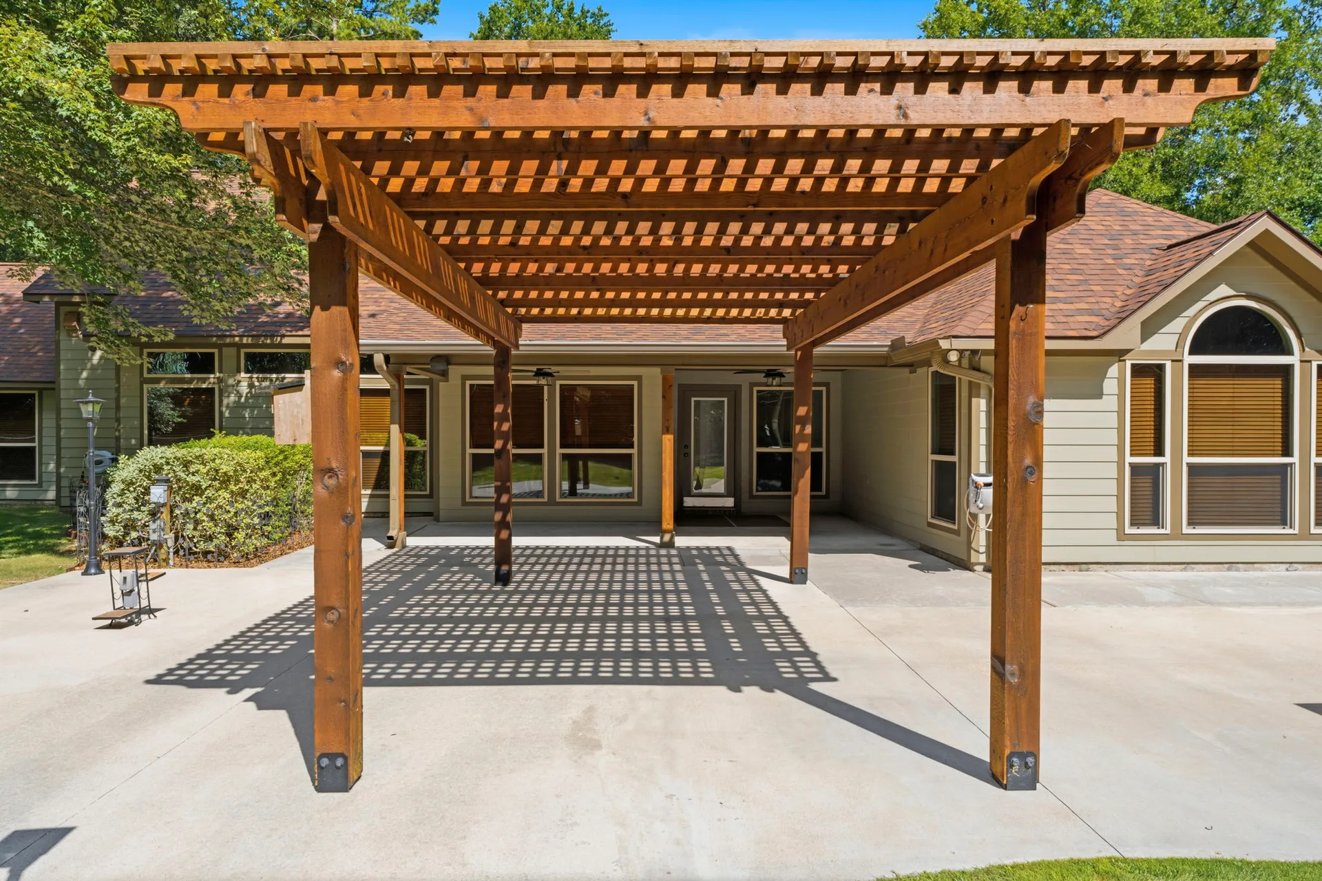 Close-up of large wood pergola attached to rear of home over concrete patio