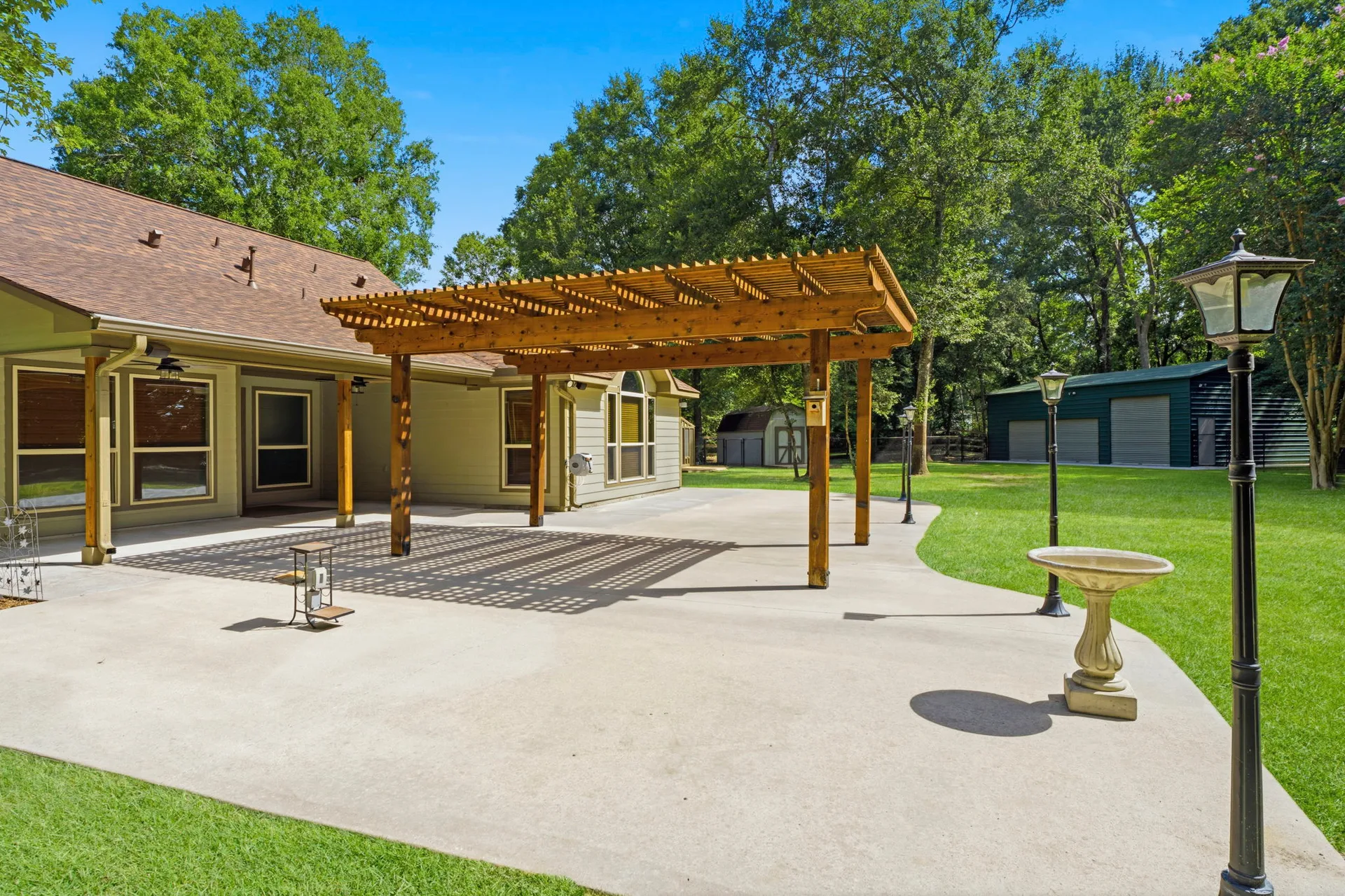 Backyard patio with pergola, lamps, and detached workshop in background