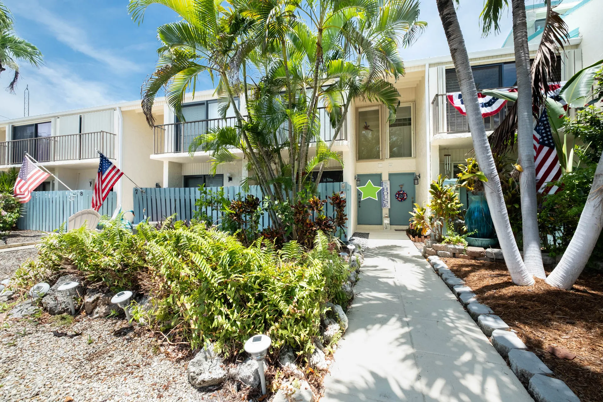 Townhouse facade with blue privacy fencing and palm trees