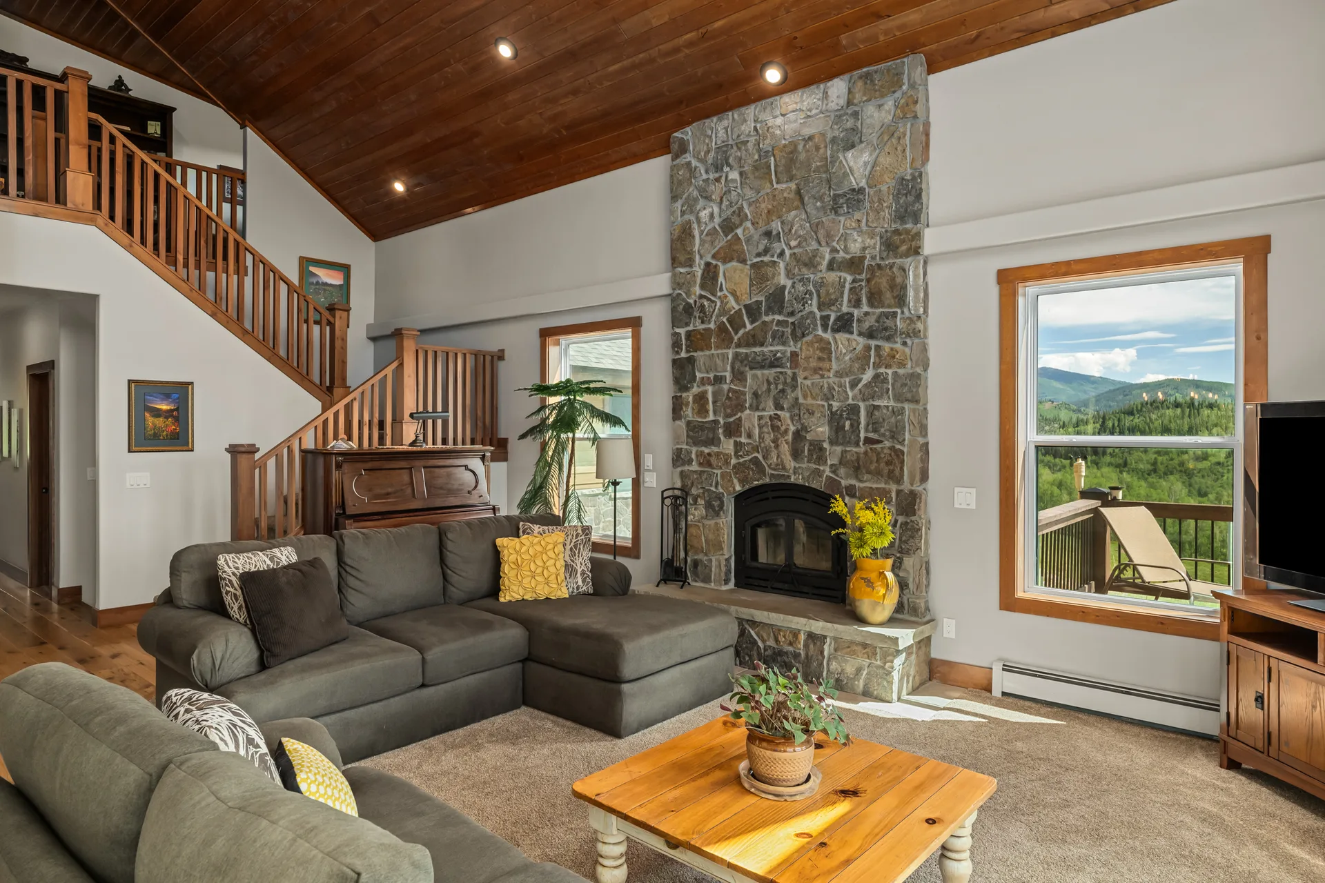 Living room with vaulted ceilings and stone fireplace framing mountain vistas