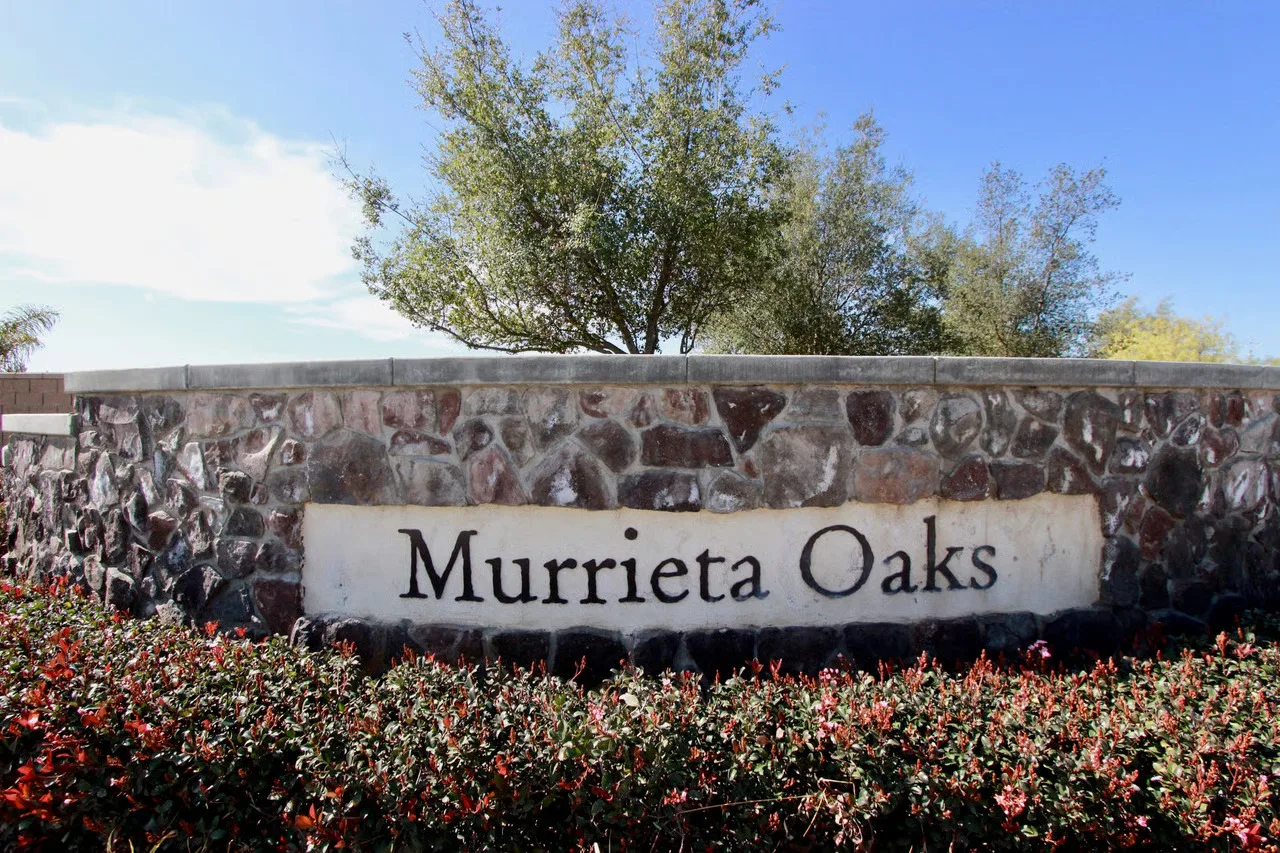 Stone entrance sign for the Murrieta Oaks community with blue sky and greenery