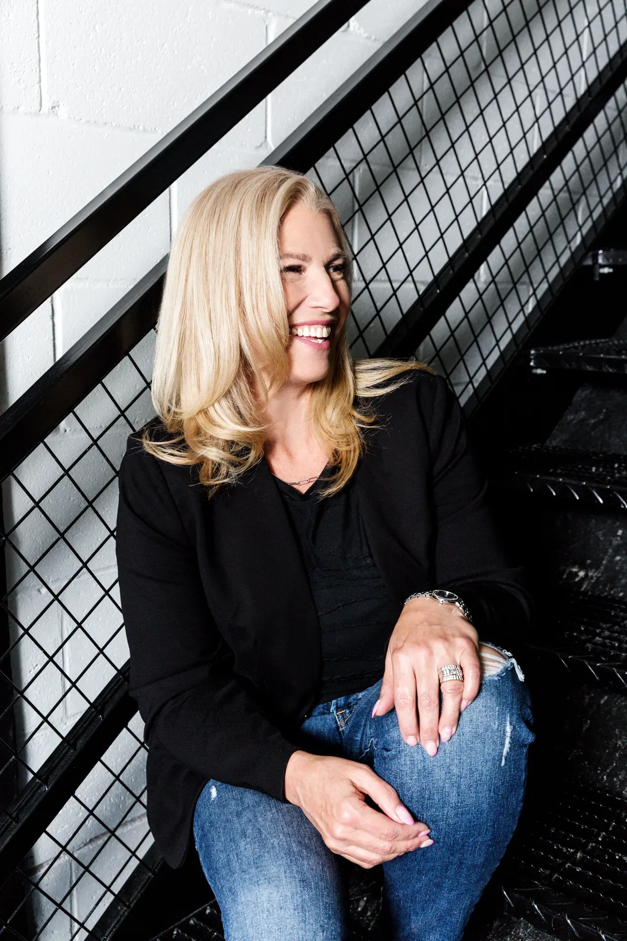 Lee Lander laughing candidly while sitting on industrial metal stairs