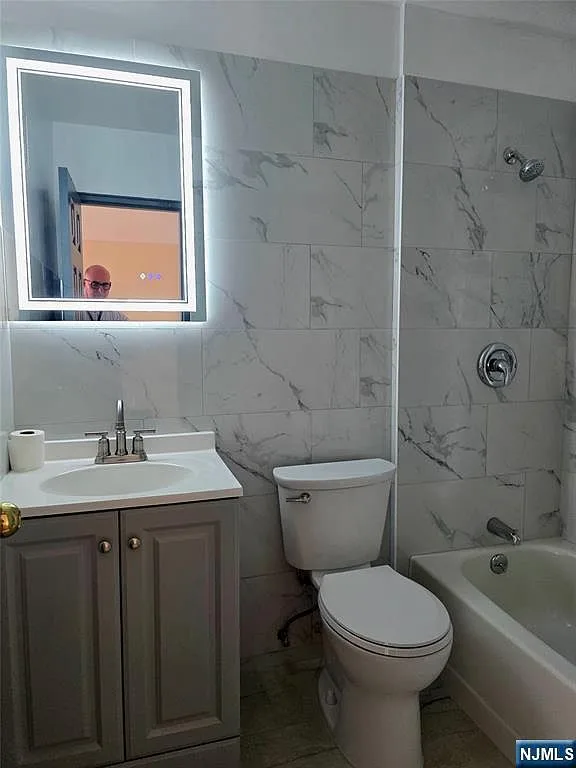 Fully renovated bathroom with marble-look tile and LED vanity mirror