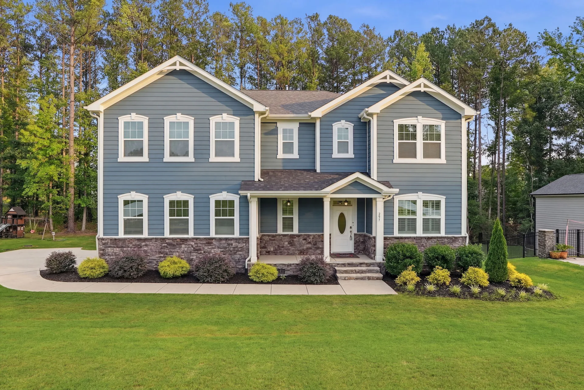 Straight-on daytime view of the front facade with blue siding and stone accents