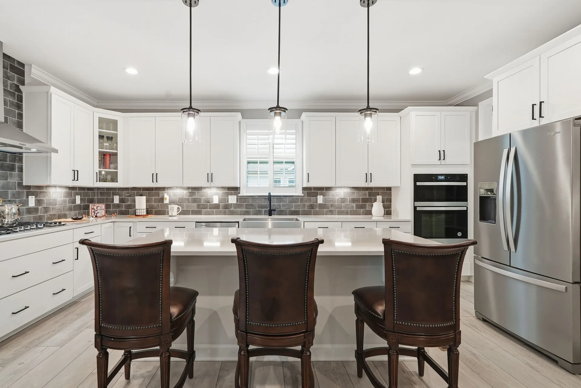 Head-on view of the kitchen island with white shaker cabinets, glass pendant lights, and quartz countertops