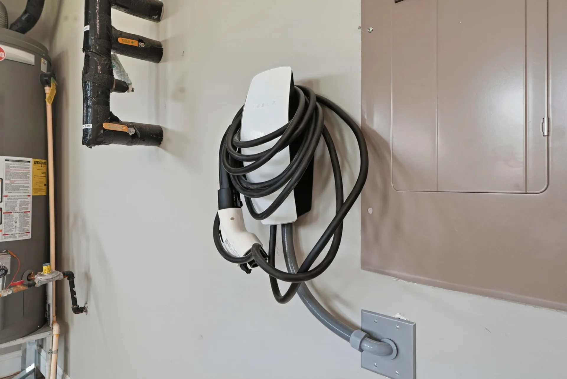 Garage interior with Tesla wall connector EV charger, water heater, and electrical panel