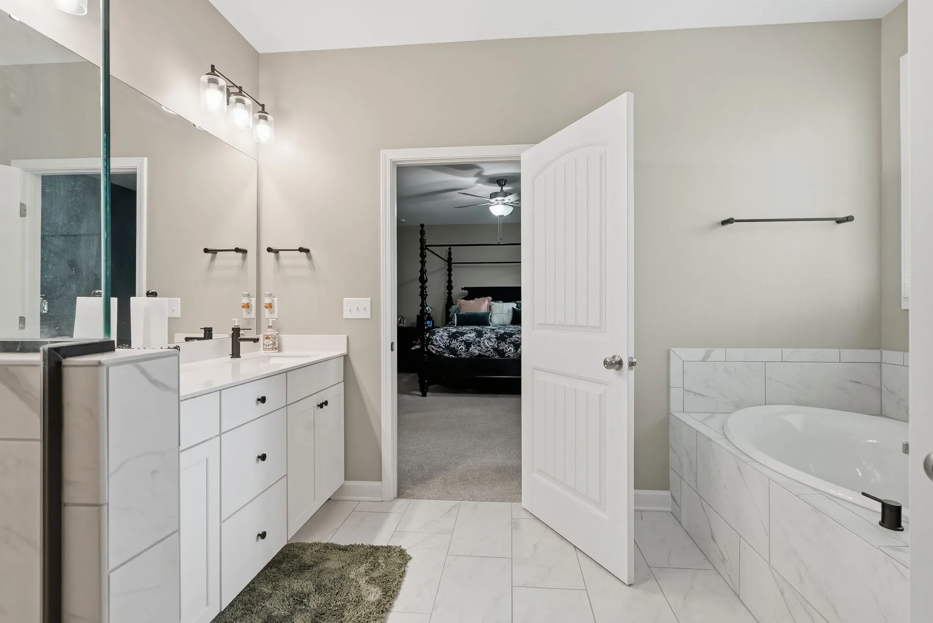 Master bathroom soaking tub with white marble-look tile surround and vanity in view
