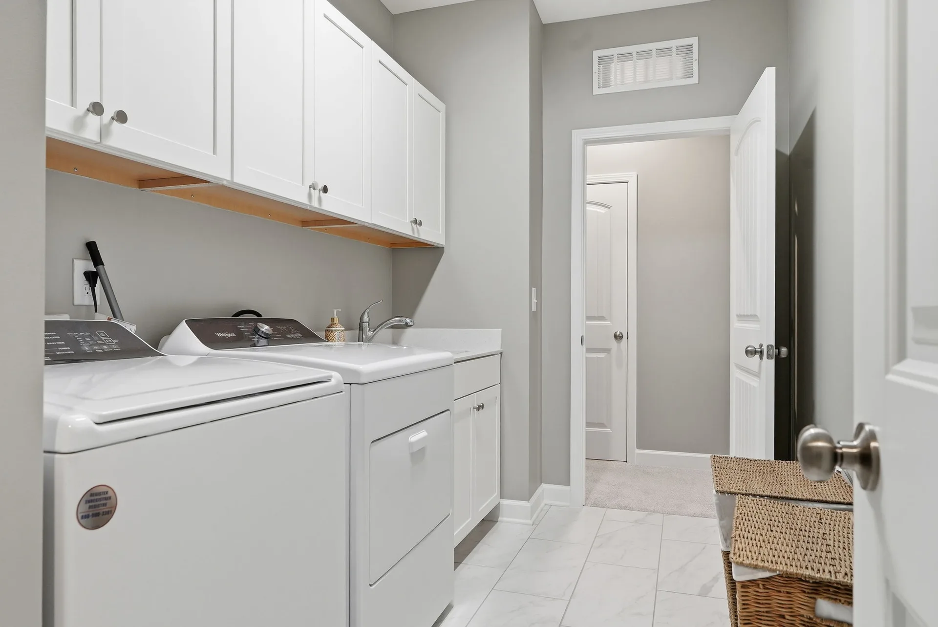 Laundry room with white cabinets, tiled floors, and sink