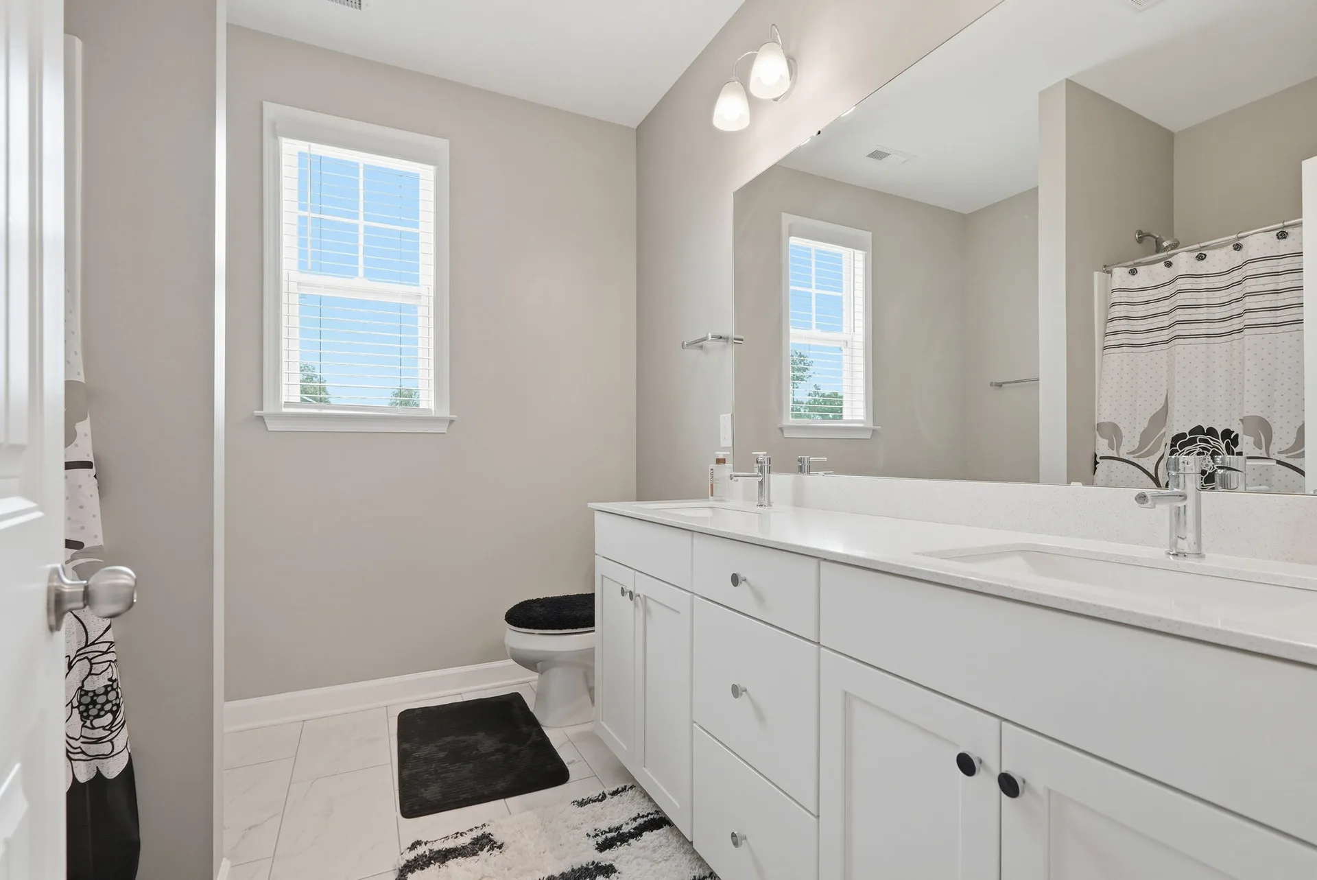 Modern bathroom with white shaker dual vanity, chrome fixtures, quartz countertop, and large mirror