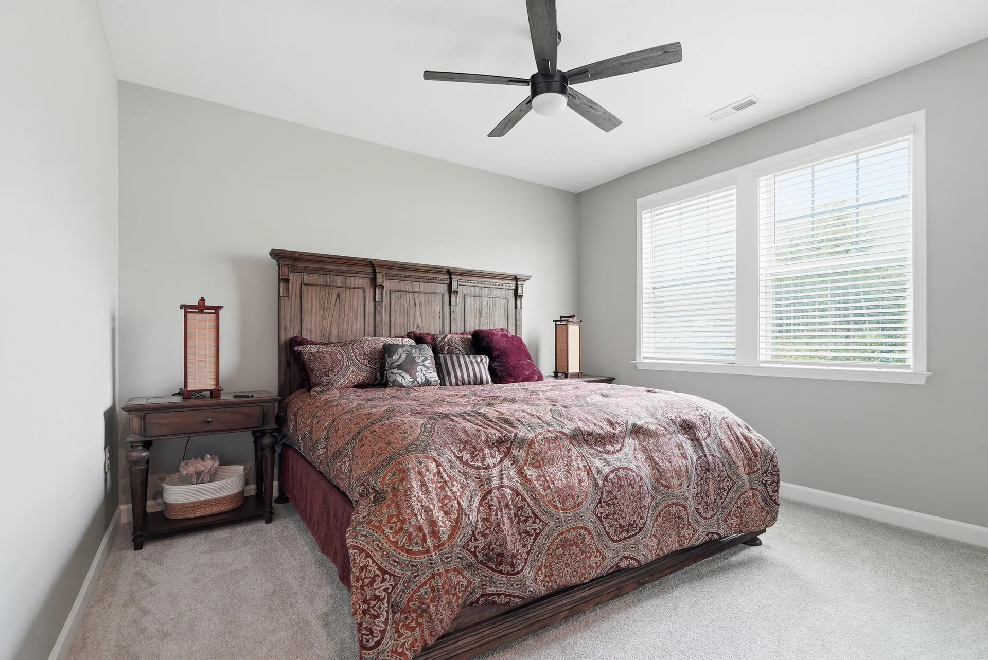 Secondary bedroom with grey walls, neutral carpet, dark wood panel bed frame, and ceiling fan