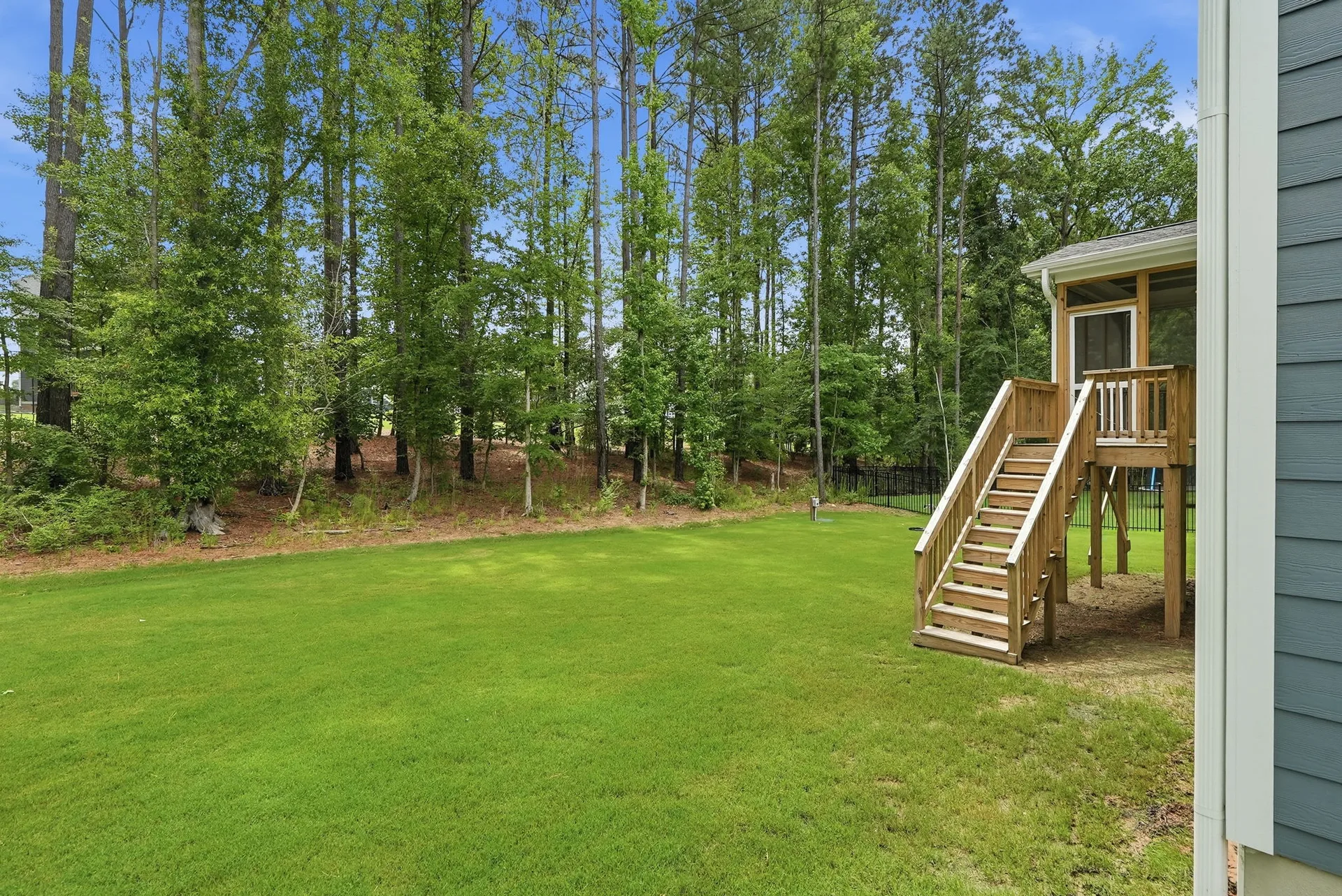 Backyard view showing raised wooden screened-in porch with staircase and gravel area