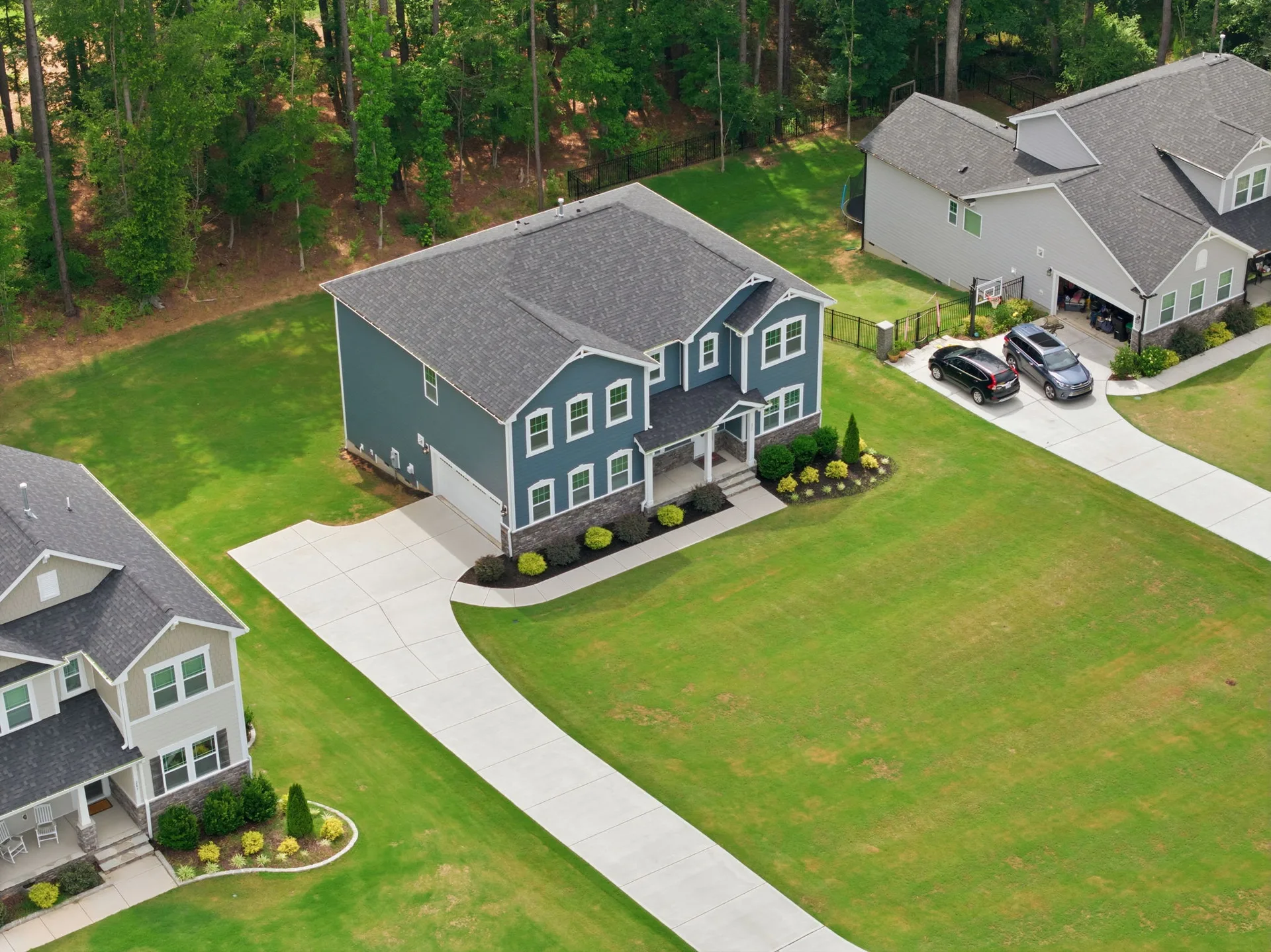 Aerial view showing the two-story home on a corner lot with wooded area in the background