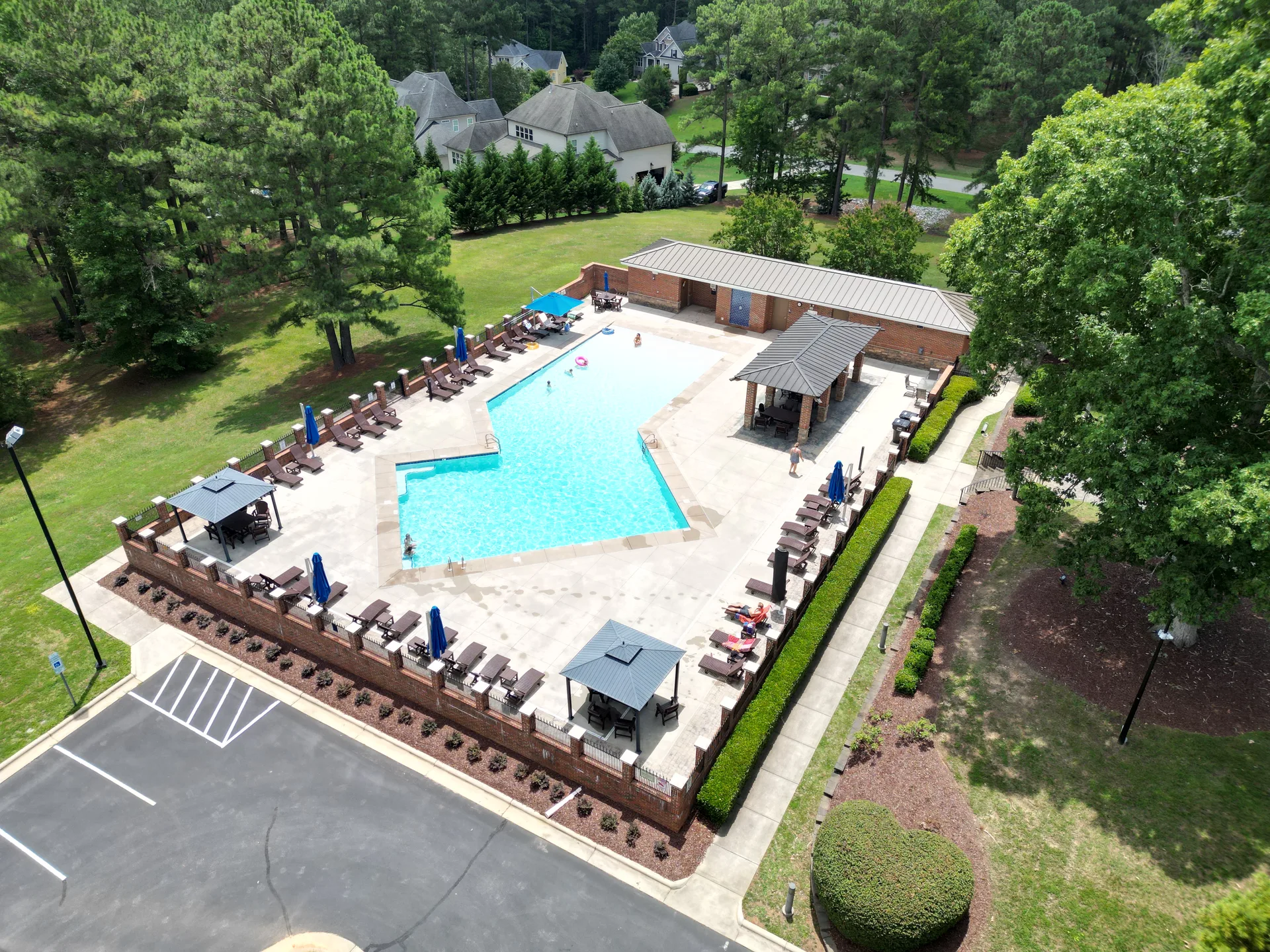 High-angle aerial view of the large community pool with brick walls, gazebos, and umbrellas