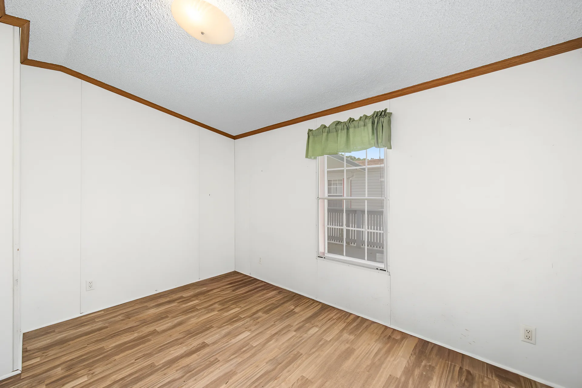 Vacant secondary bedroom with white walls, wood-tone trim, and natural window light