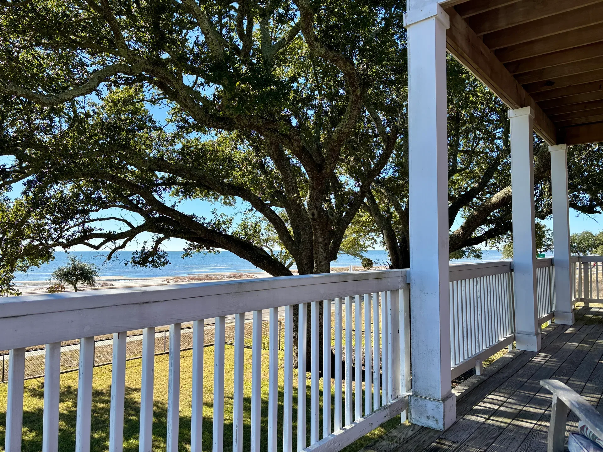 View of a peaceful coastal landscape with a large oak tree and the ocean visible from a wooden residential porch