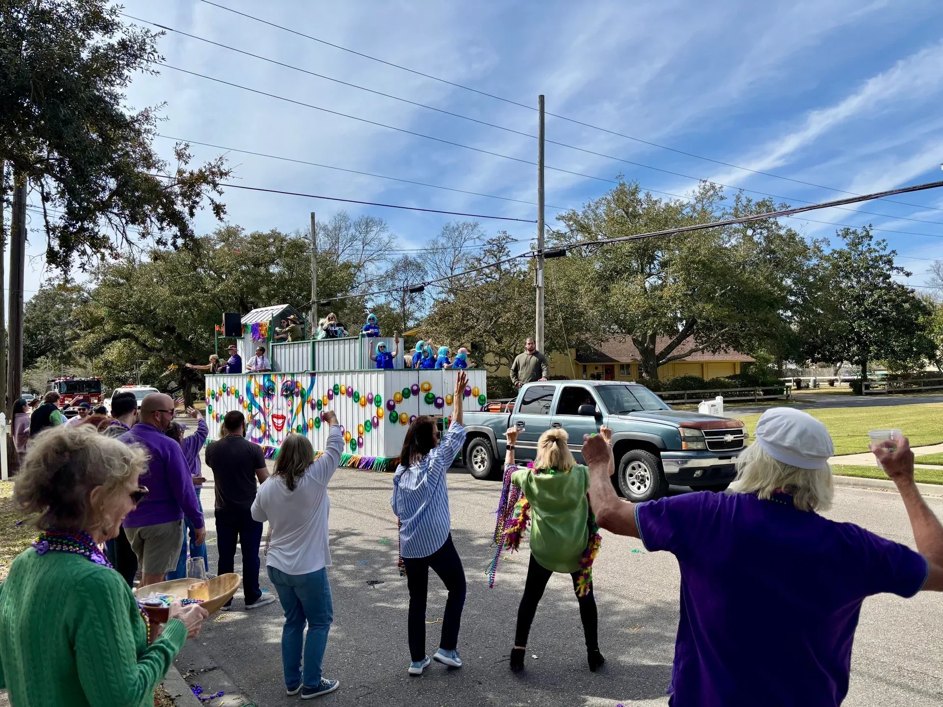 A group of people watch a Mardi Gras parade float passing by on a sunny day