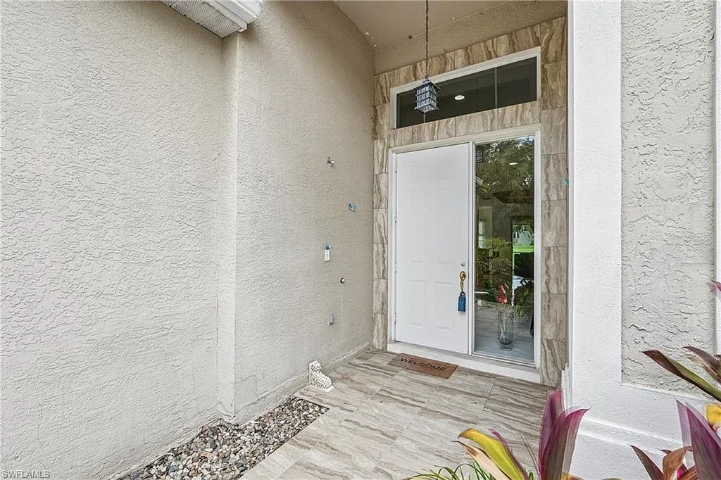 Front entry with stucco archway, white panel door, and tropical landscaping