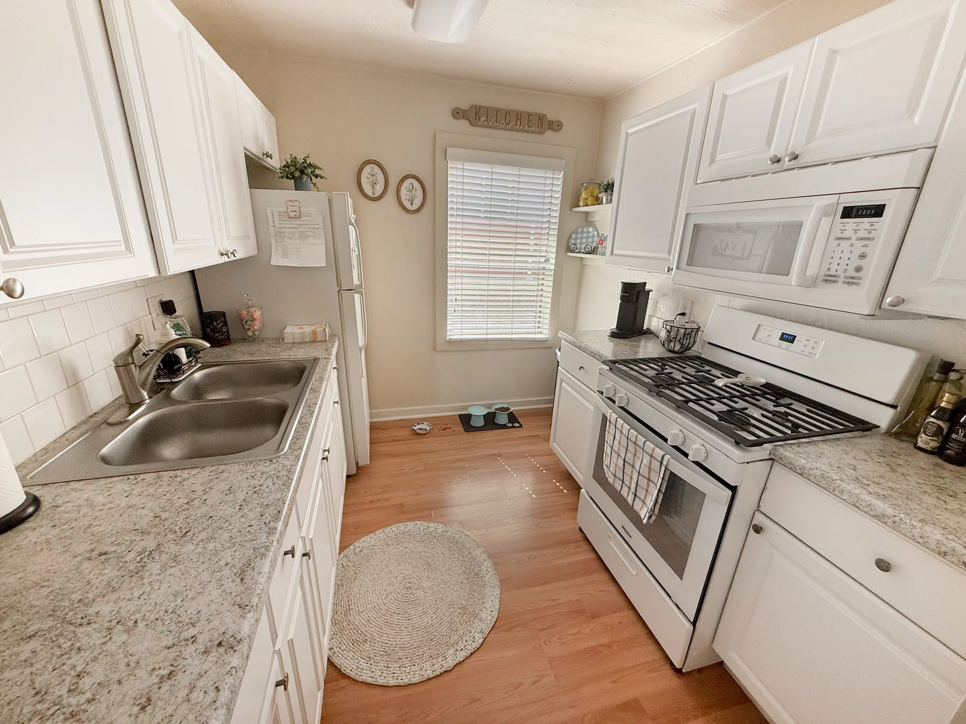 Compact galley kitchen with white cabinets and wood-look flooring