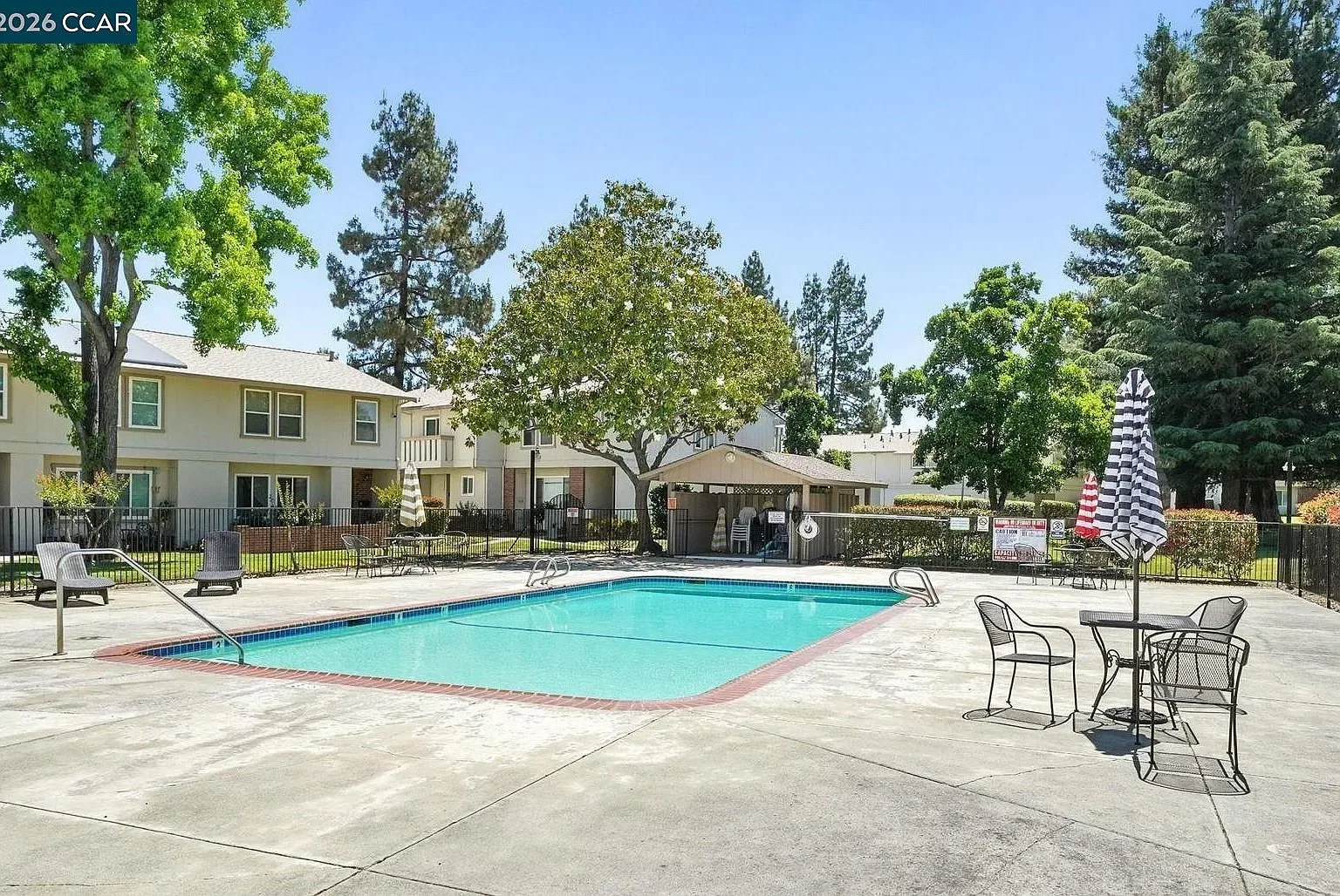Community swimming pool area with patio furniture and blue sky