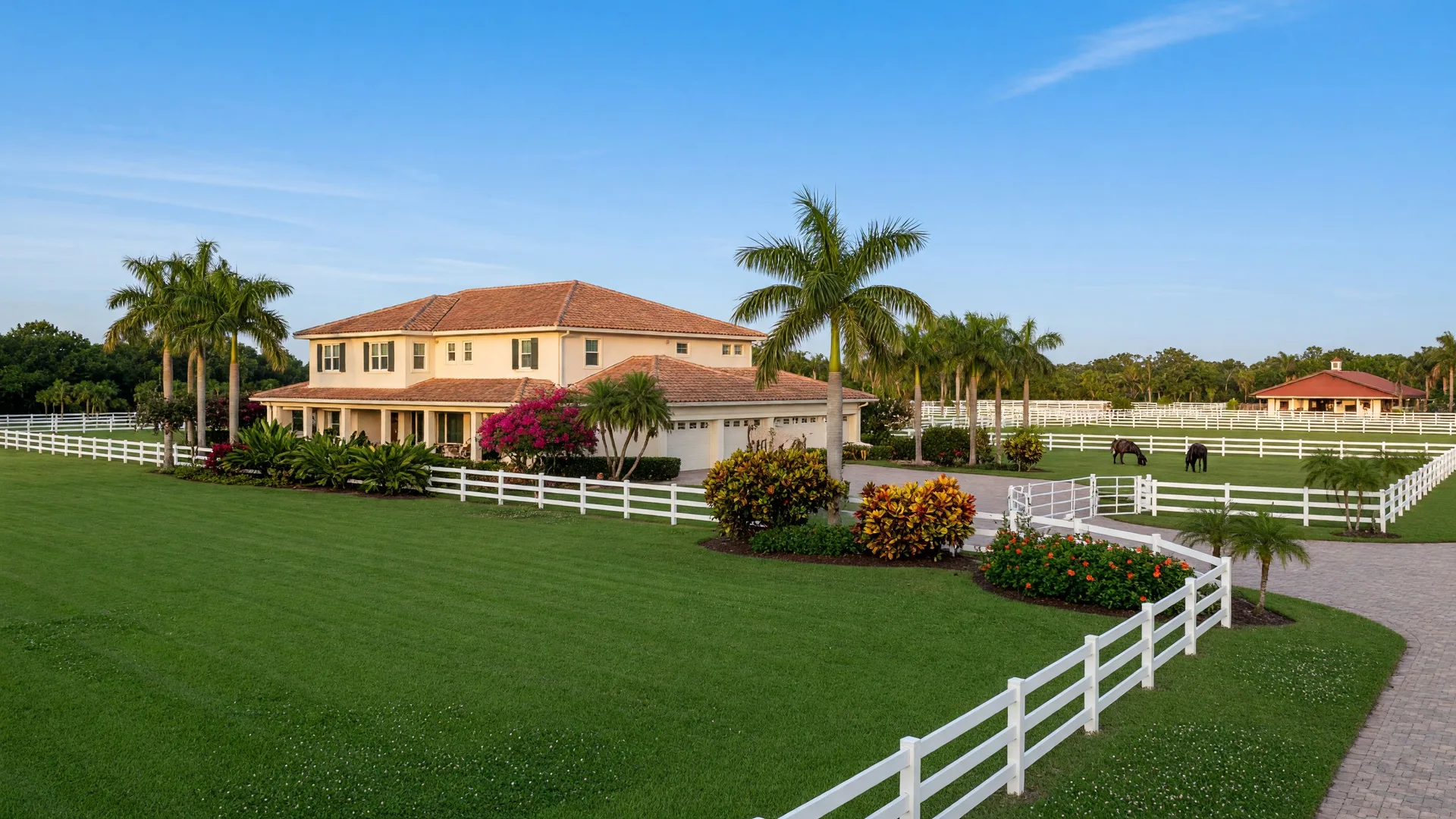 A spacious equestrian estate in Wellington with white fencing, green lawn, and tropical landscaping
