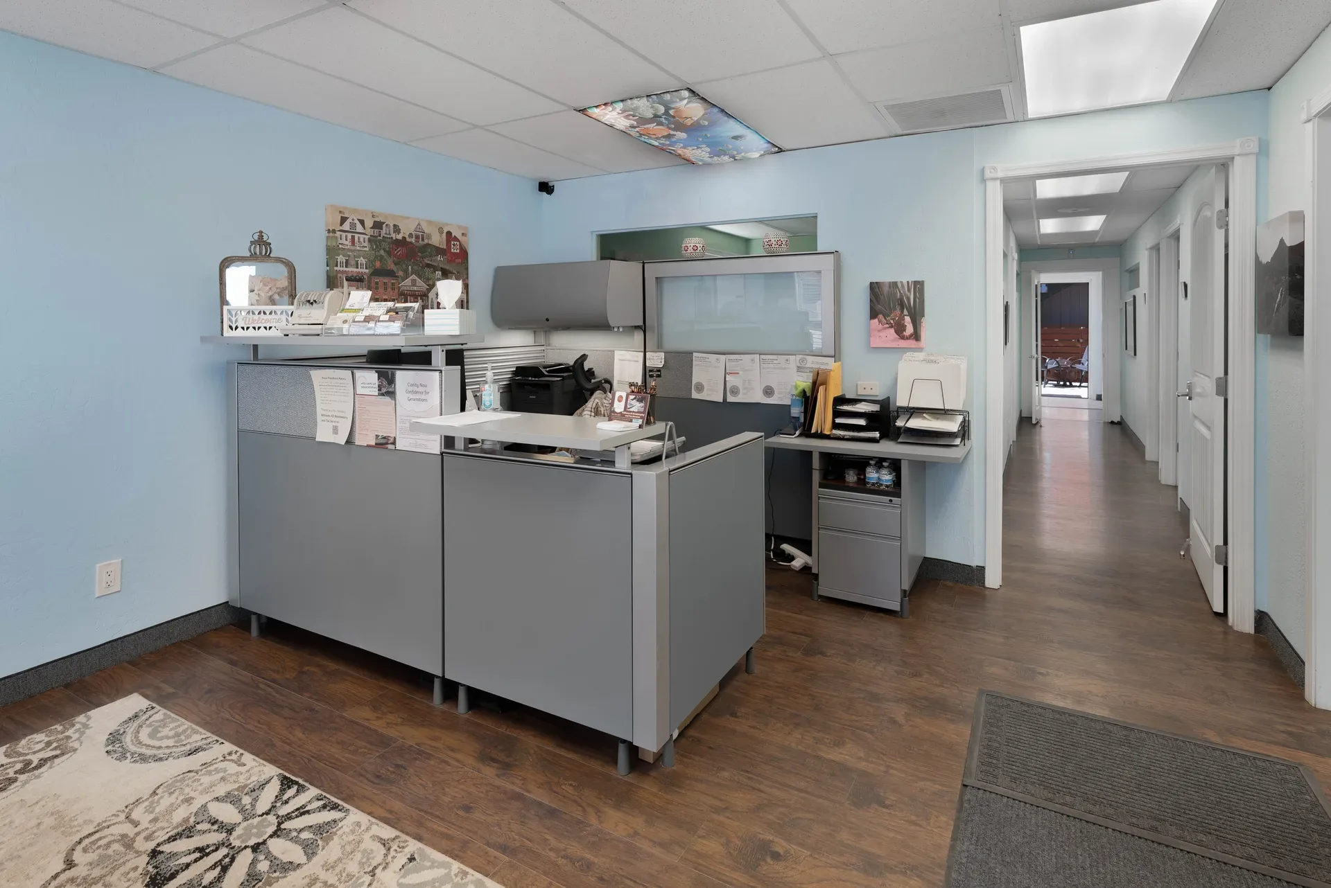 Wide-angle office reception area with cubicle dividers, reception desk, and printers