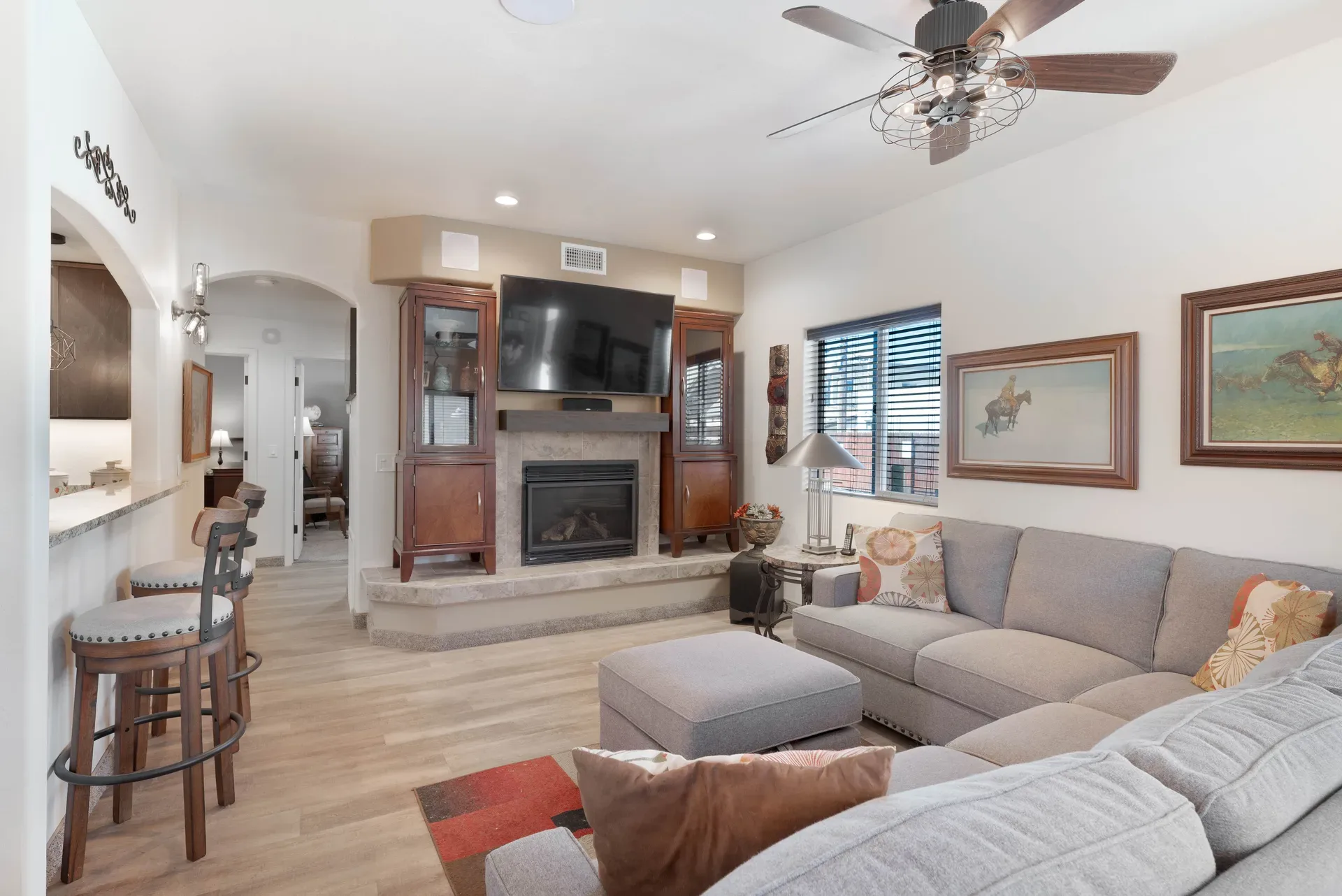 Living room with stone fireplace, wood-tone flooring, and kitchen bar seating