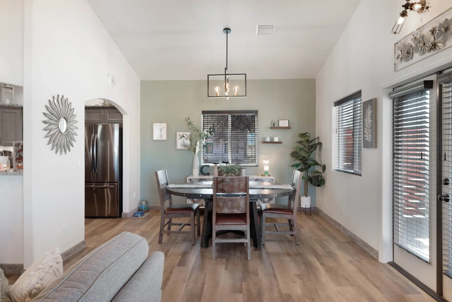 Open-concept dining area with wood plank flooring, sage accent wall, and vaulted ceilings