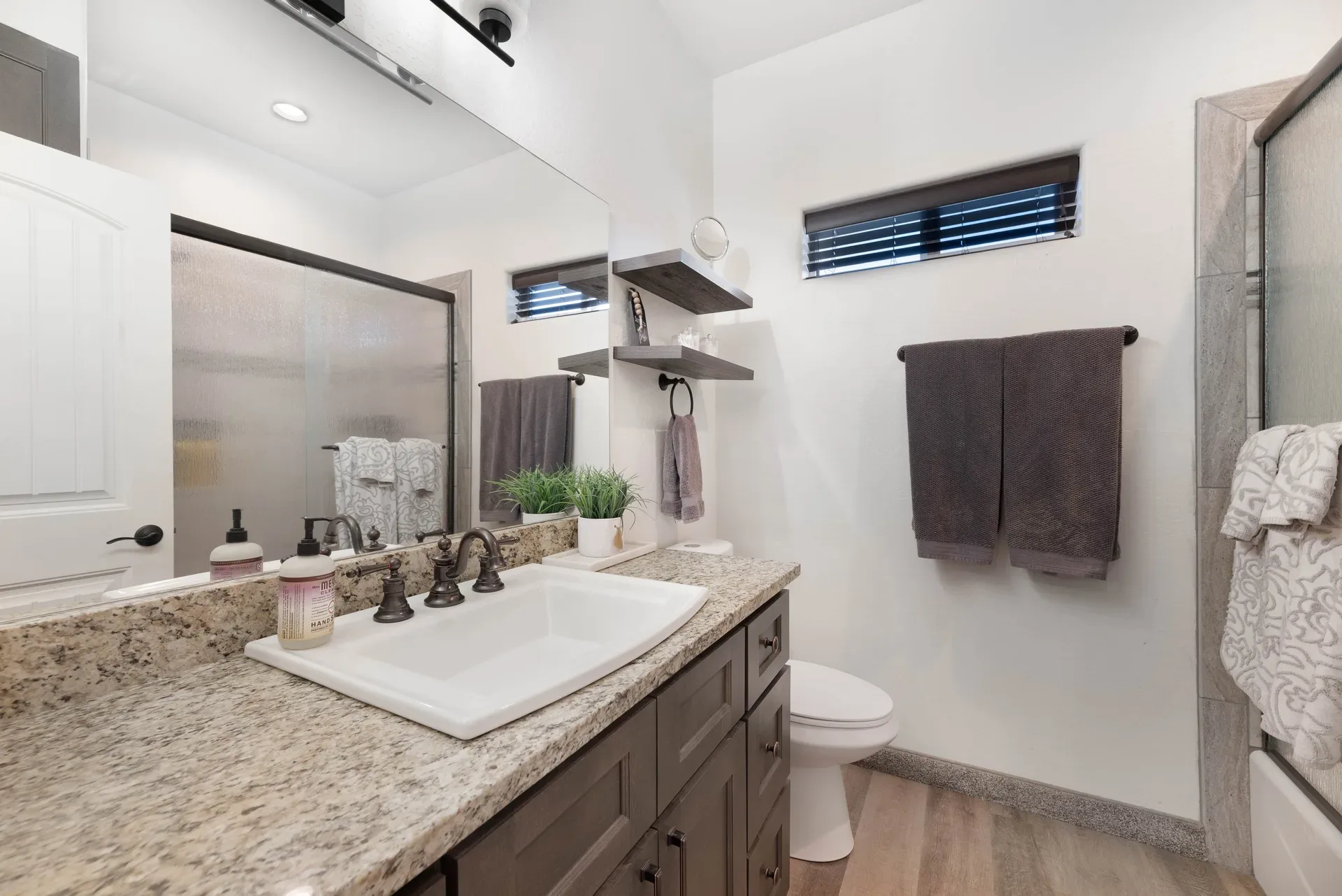 Contemporary bathroom with dark gray cabinets, granite countertop, and brushed bronze fixtures