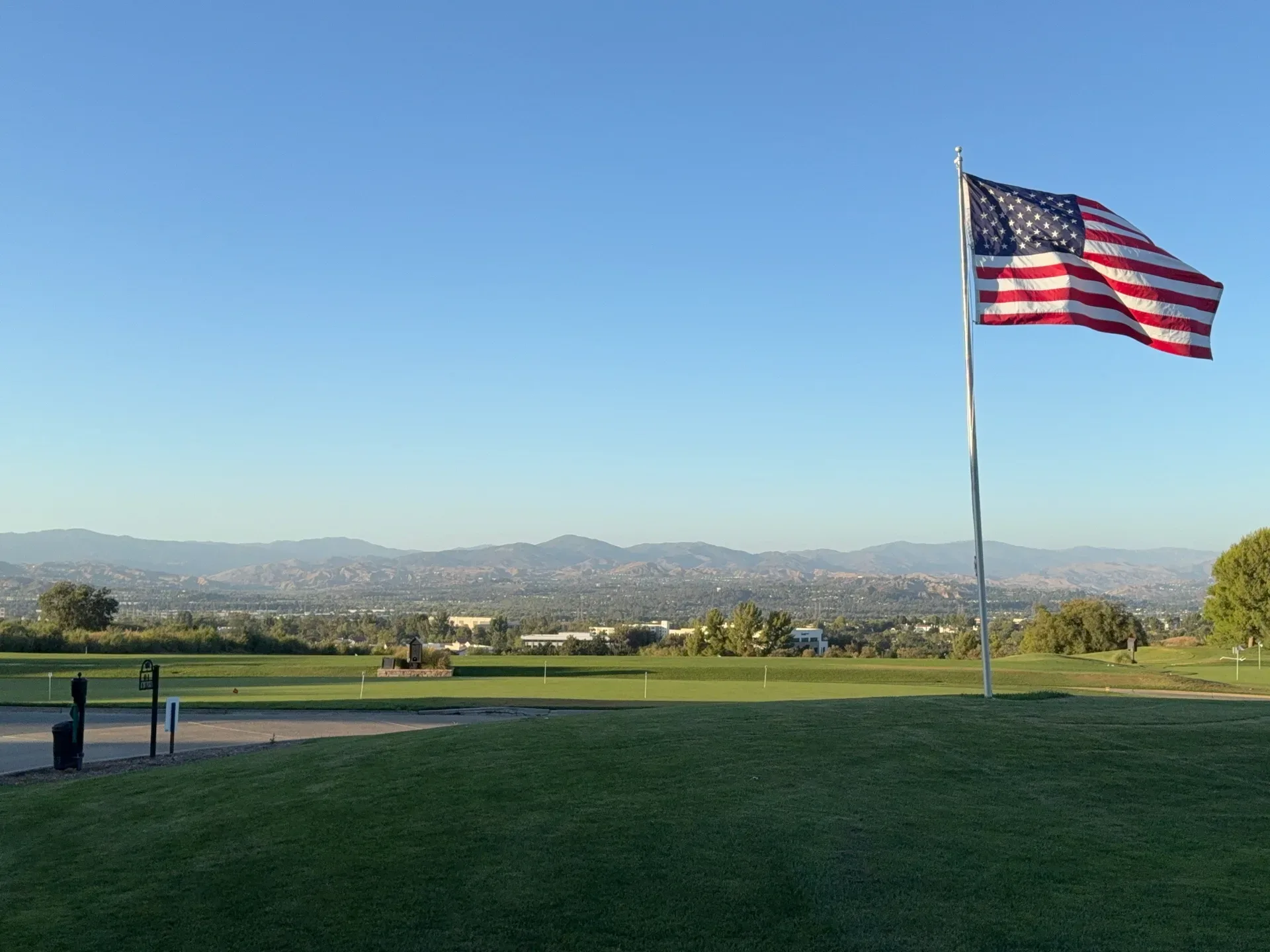 An American flag flies over a green landscape with distant mountains under a clear blue sky