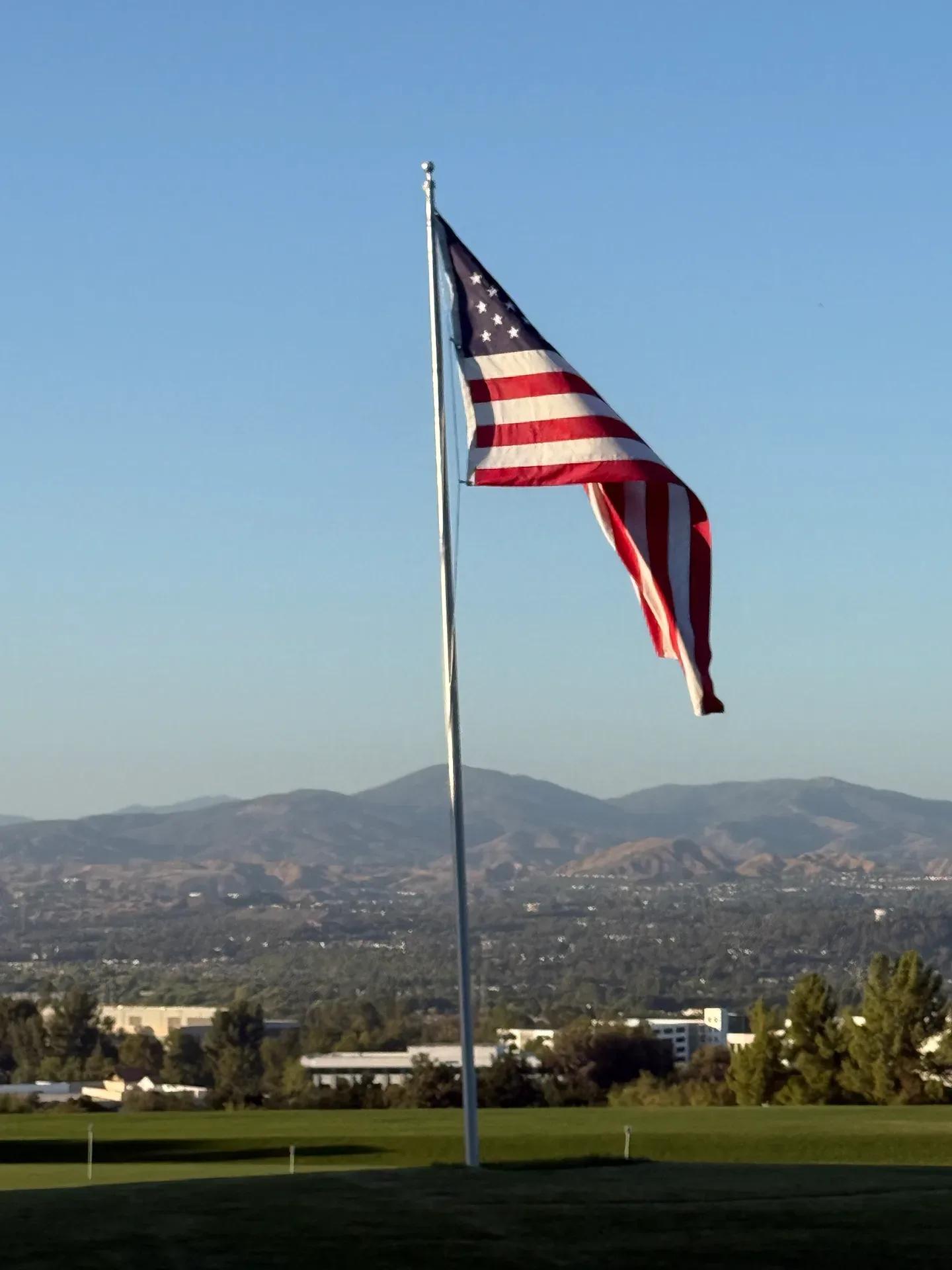 An American flag waves against a clear blue sky with mountains in the background