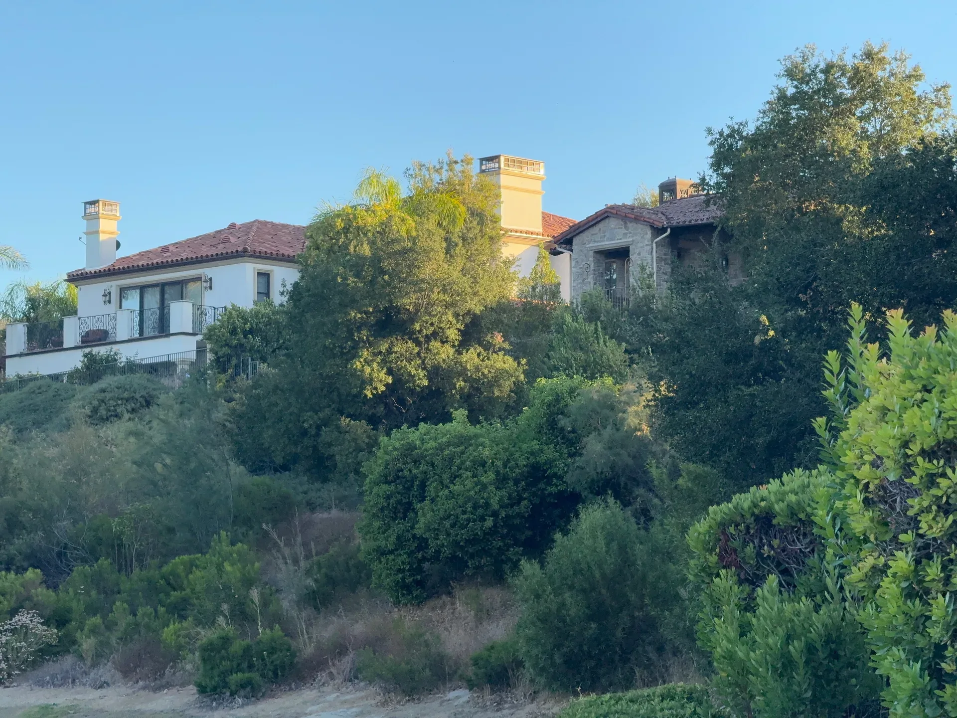 A Mediterranean-style home with a red-tiled roof sits nestled among lush trees and greenery in Southern California