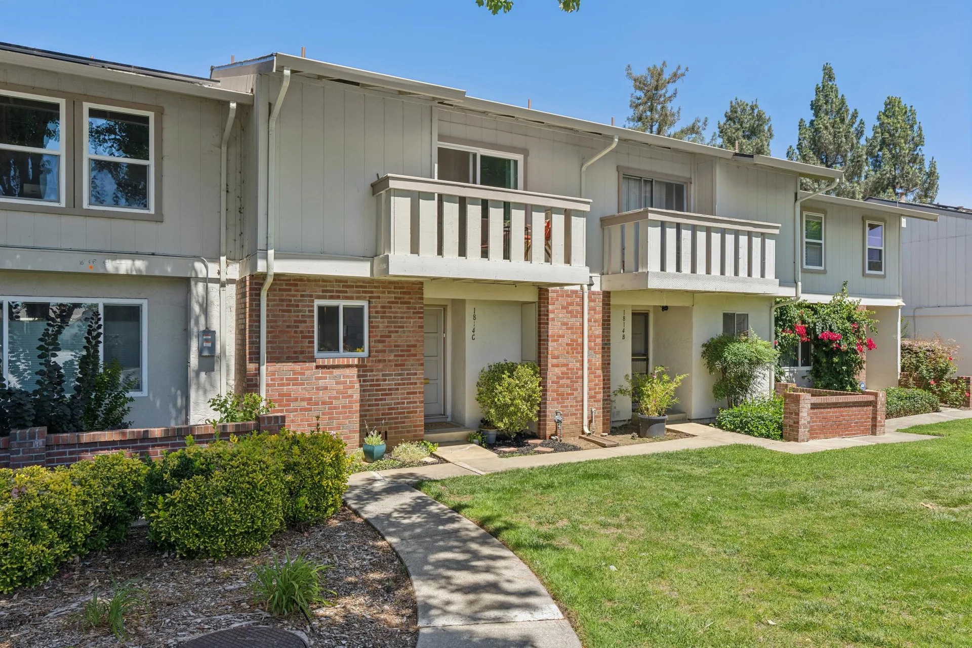 Two-story townhome facade with brick veneer siding, concrete walkways, and second-story balconies