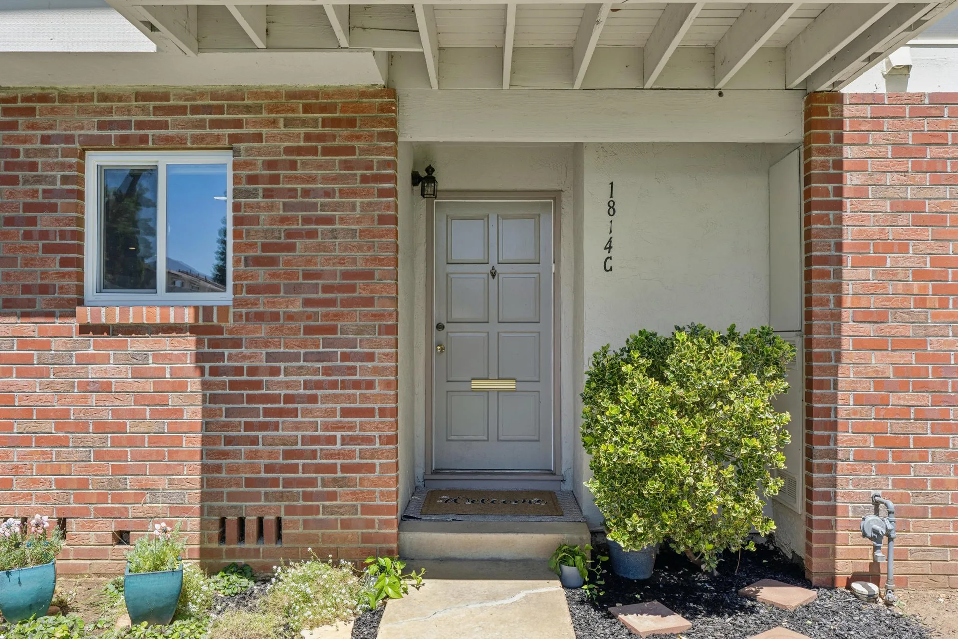 Front door with grey painted finish, blue planters, and brick siding