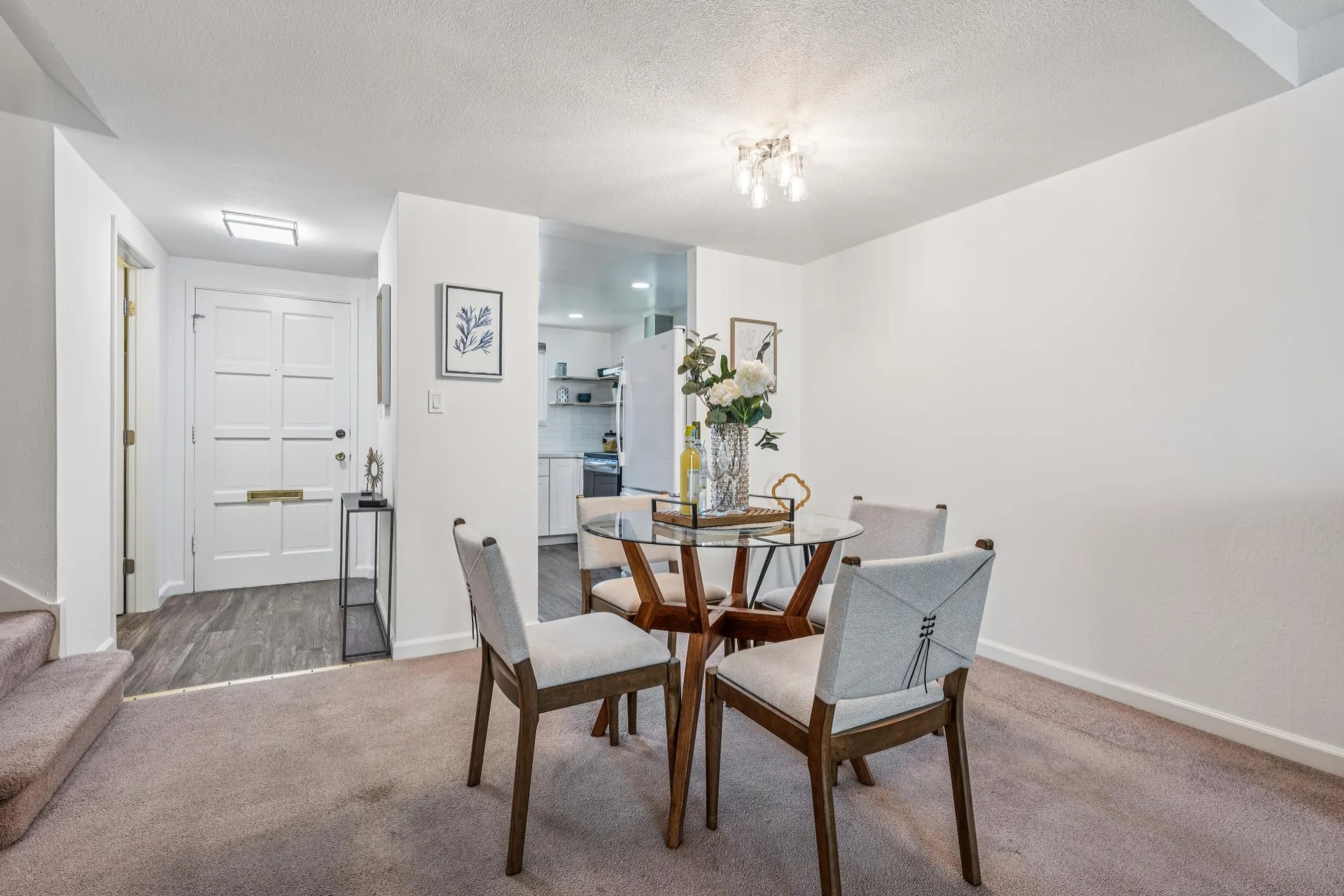 Dining area facing the front entryway with glass-top table and kitchen view