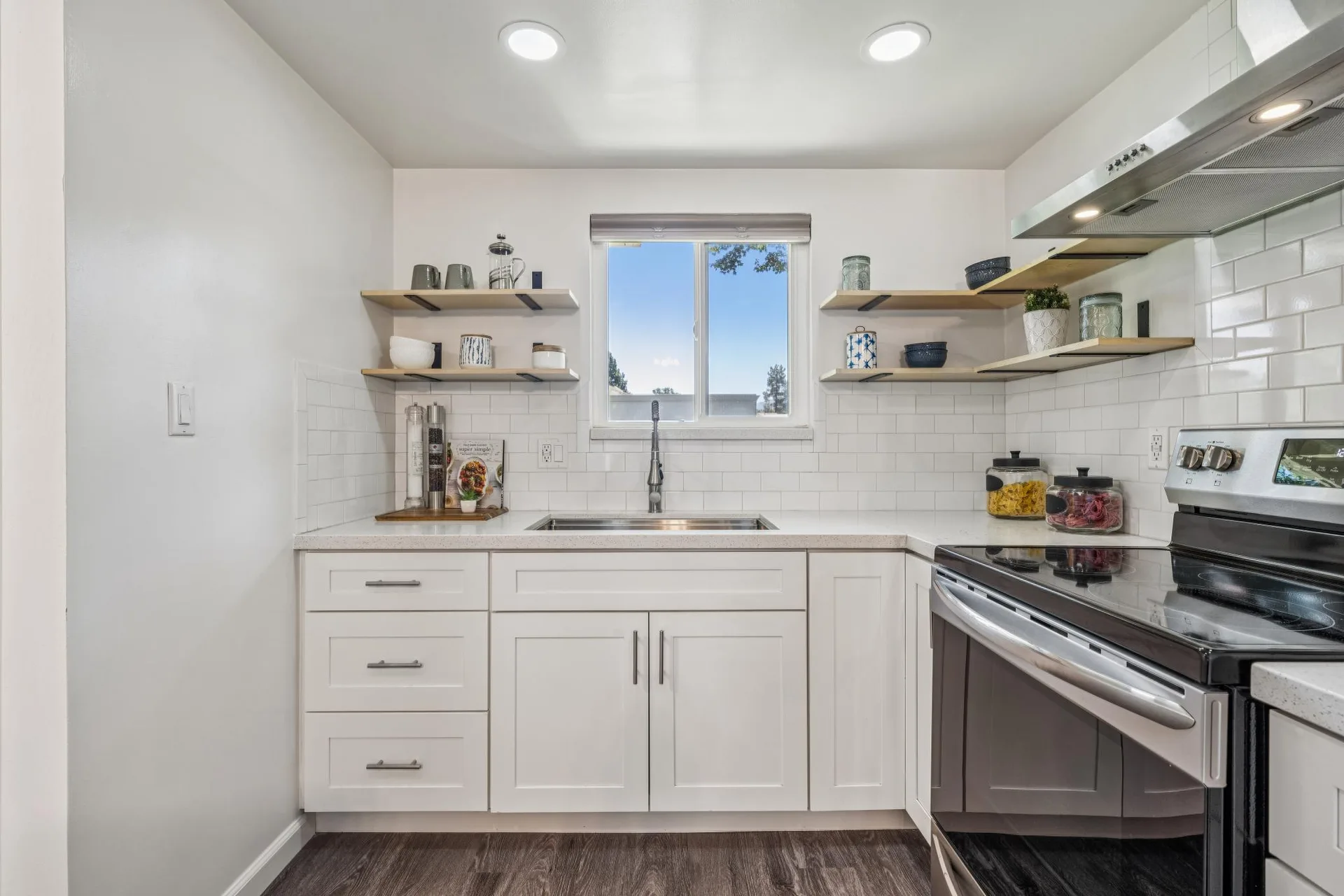 Kitchen head-on view of sink and stove with white cabinetry and open shelving