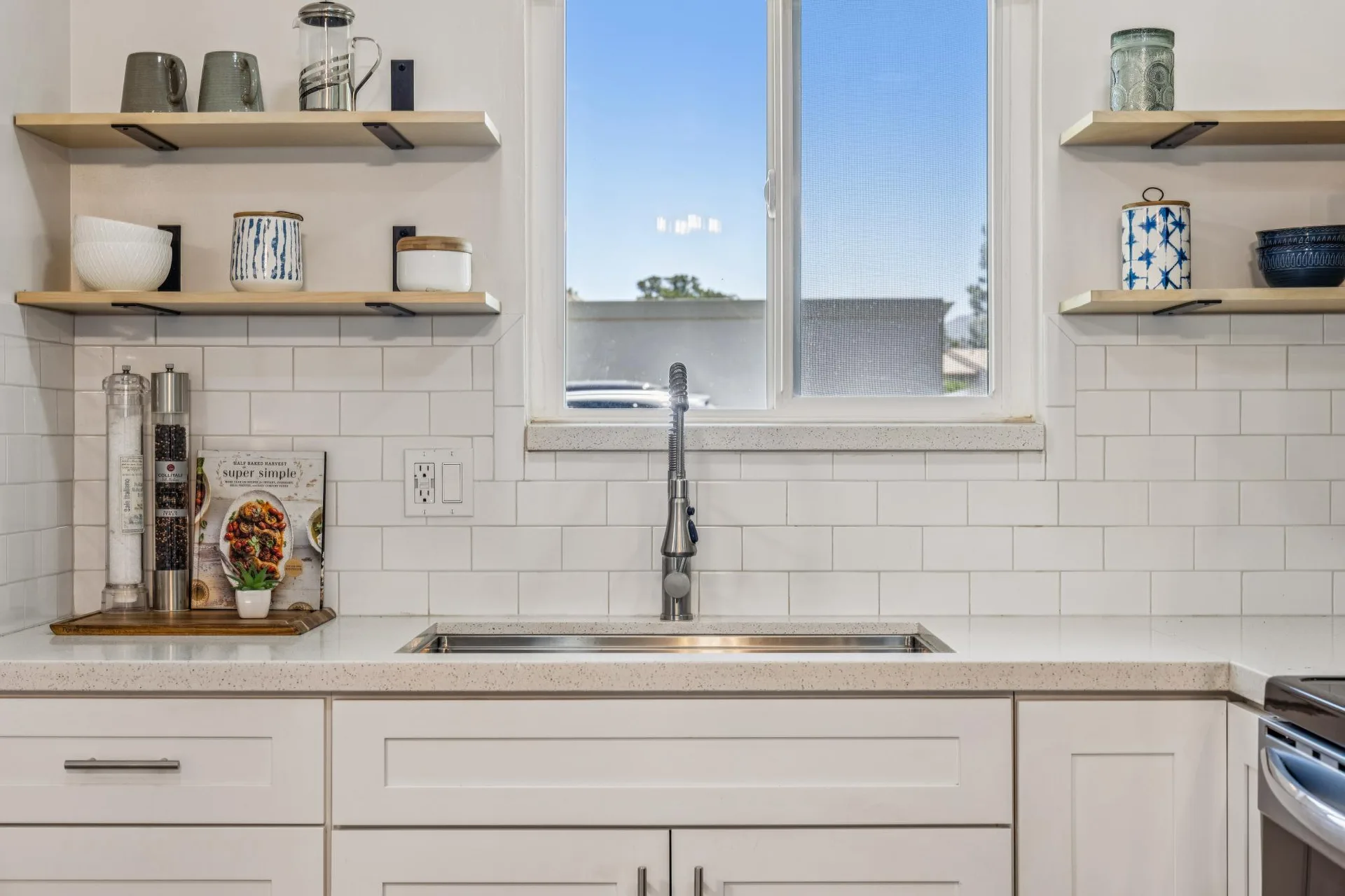 Kitchen sink area with white countertops, subway tile backsplash, and wood floating shelves