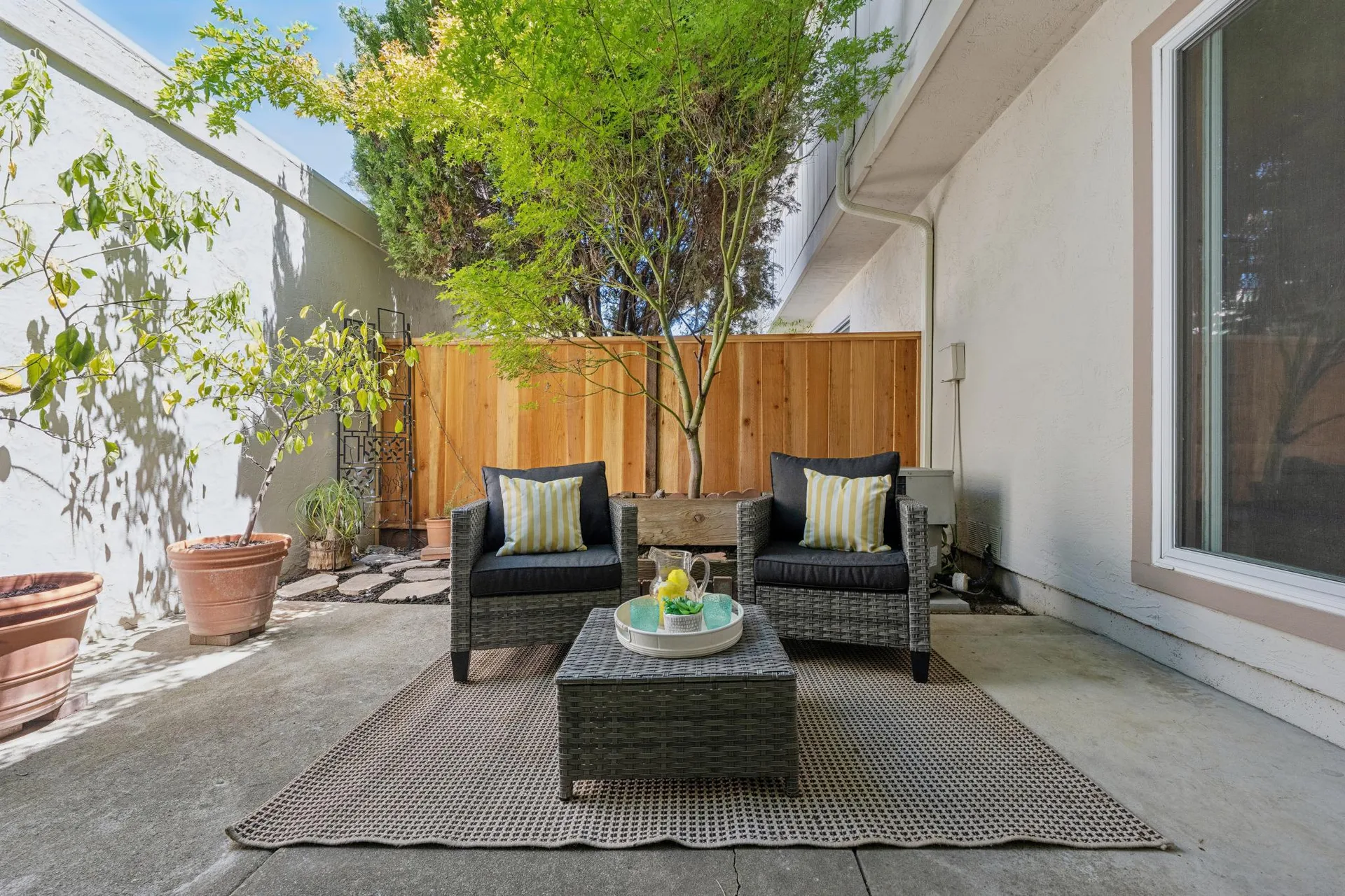 Patio with concrete slab, wood fence, striped pillows, and tree canopy shade