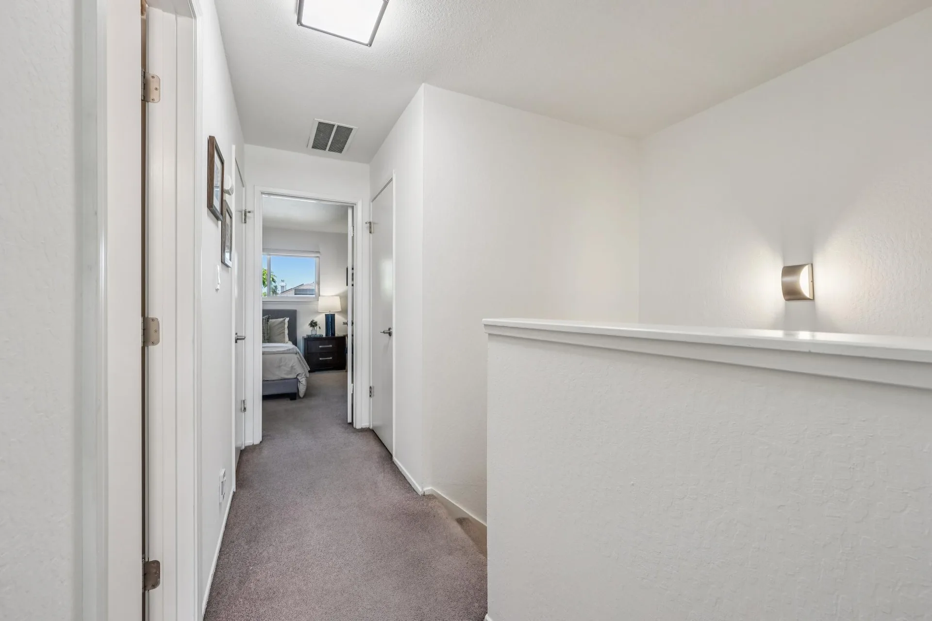 Upstairs hallway landing with carpet, neutral walls, and wall sconce